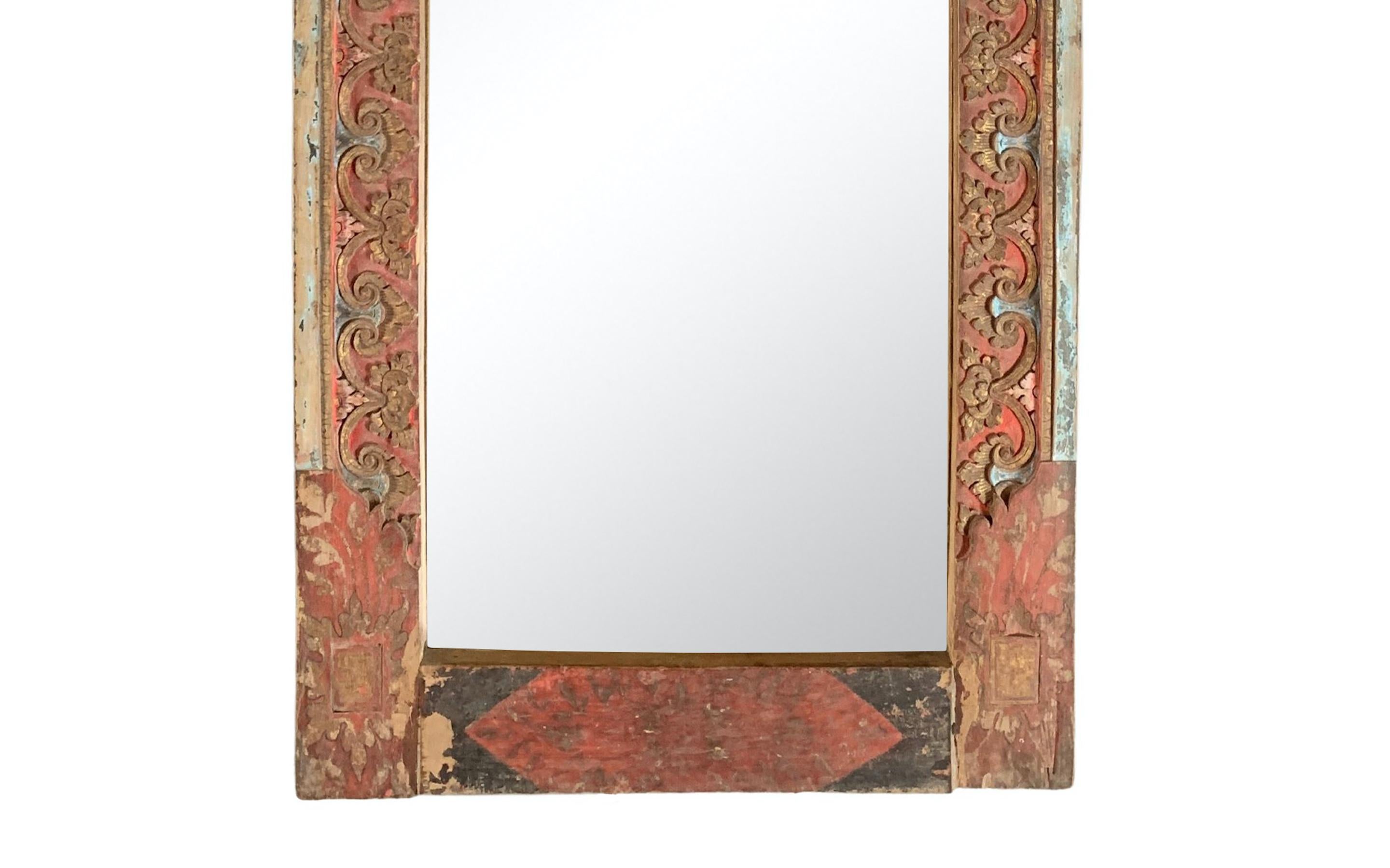 Dieser Spiegel wurde um die Mitte des 20. Jahrhunderts auf der Insel Bali gefertigt und zeichnet sich durch wunderbare Balinesische geschnitzte Details und eine polychrome Oberfläche in Rot, Schwarz und Gold aus. An der Rückseite des Spiegels ist