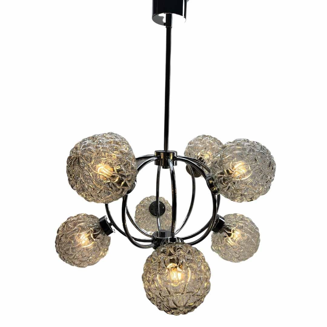 From the range by the Massive Company, this center-light features 8 lamps  on a central chromed stem. Each lamp has a fitting on a chromed plate, and each holds a round globular shade of clear glass sculpted to produce a series of concentric circles