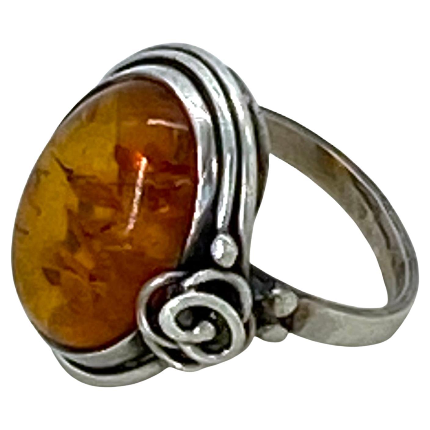 Si tratta di un anello d'argento vintage in ambra baltica. Il cabochon d'ambra di 1 x 0,63 pollici è incastonato in una cornice d'argento sterling con decorazione floreale su un lato. Il timbro .925 si trova sul bordo esterno dell'anello.

La nostra