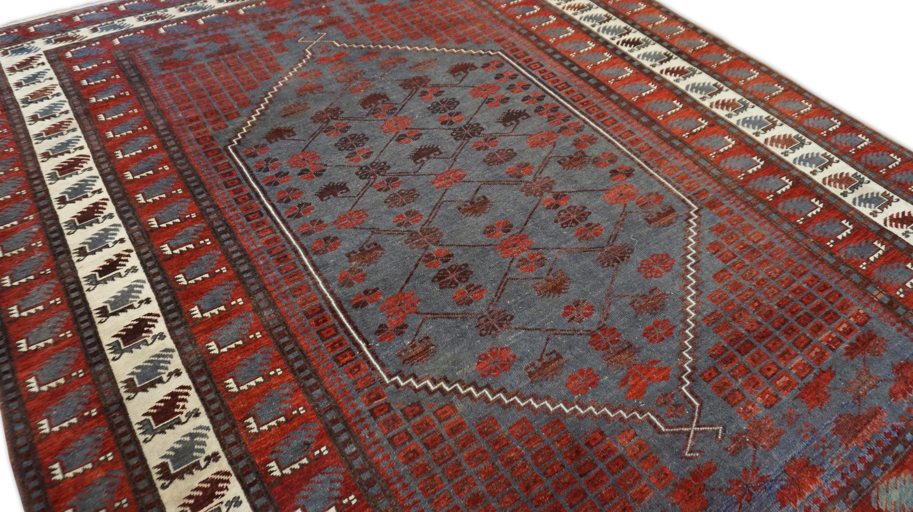 This vintage hand-knotted wool rug features a striking tribal aesthetic rooted in traditional village weaving. Rug is anchored by a deep Red field with a large stepped hexagonal medallion filled with stylized floral motifs arranged in a symmetric,