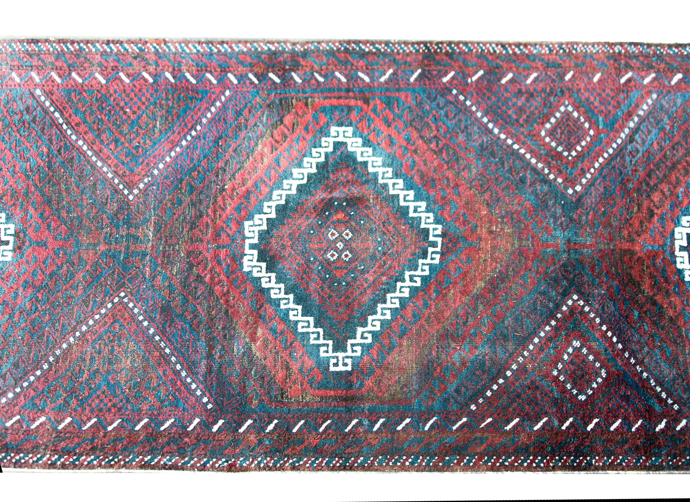 A wonderful vintage Afghani Baluchi runner with three large diamond medallions woven with repeated crimson and black stylized scrolling vine motif, and surrounded by a border with multiple petite floral patterned stripes woven in similar colors as