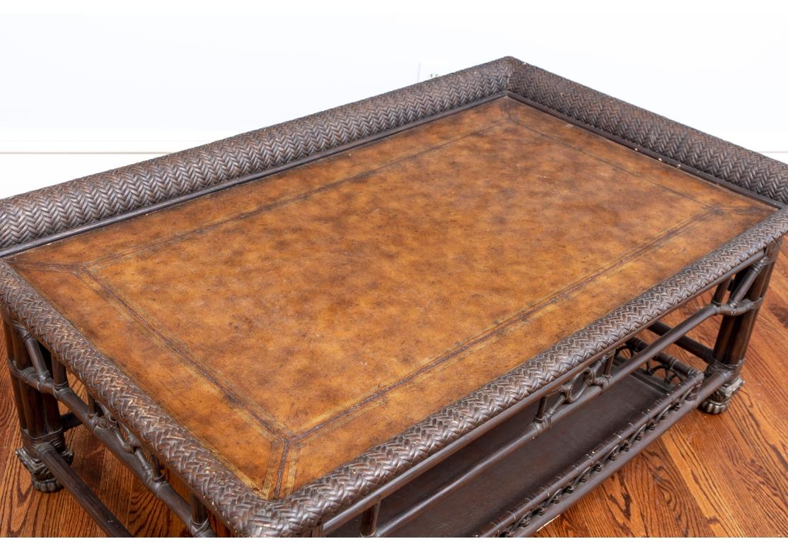 La estructura rectangular de bambú, teñida de oscuro, tiene una parte superior en forma de bandeja tejida con cuero labrado. Un delantal de bambú calado sobre un nivel inferior en forma de bandeja con los lados entrelazados. Levantado sobre pies