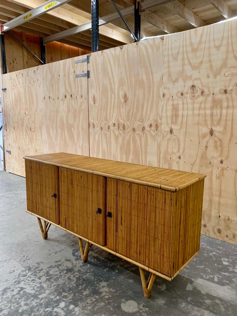 Vintage French bamboo and rattan credenza or sideboard elegantly lifted from the floor on V-shaped legs. Hidden behind the 3 doors is one large room and a small room in which both have one shelf. The buffet is in very good condition and will add