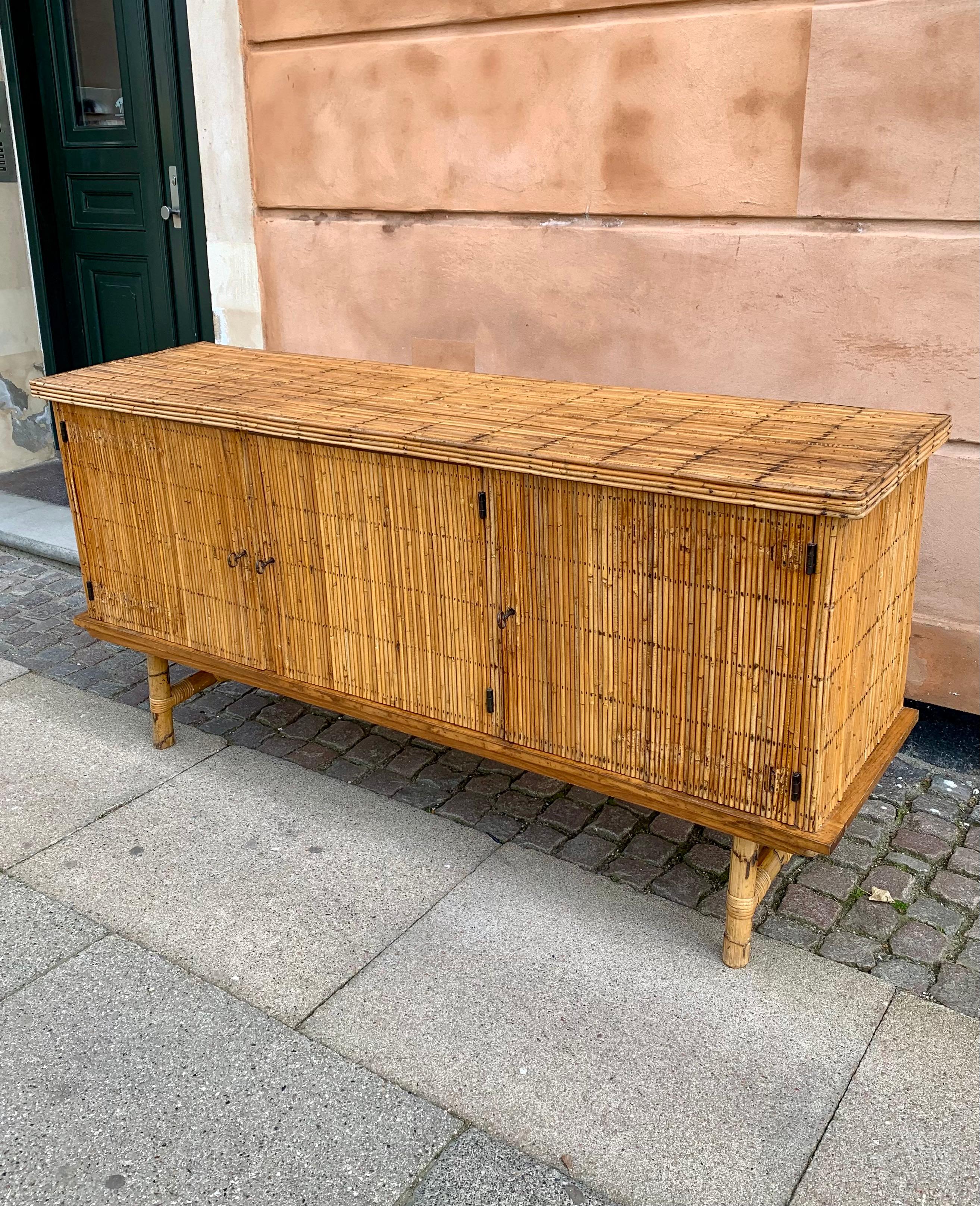 Vintage French bamboo and rattan credenza from the 1970s. The sideboard is elegantly lifted from the floor on sturdy bamboo legs and hidden behind the 3 doors are three rooms in which two of them have a shelf. The buffet is in very good condition