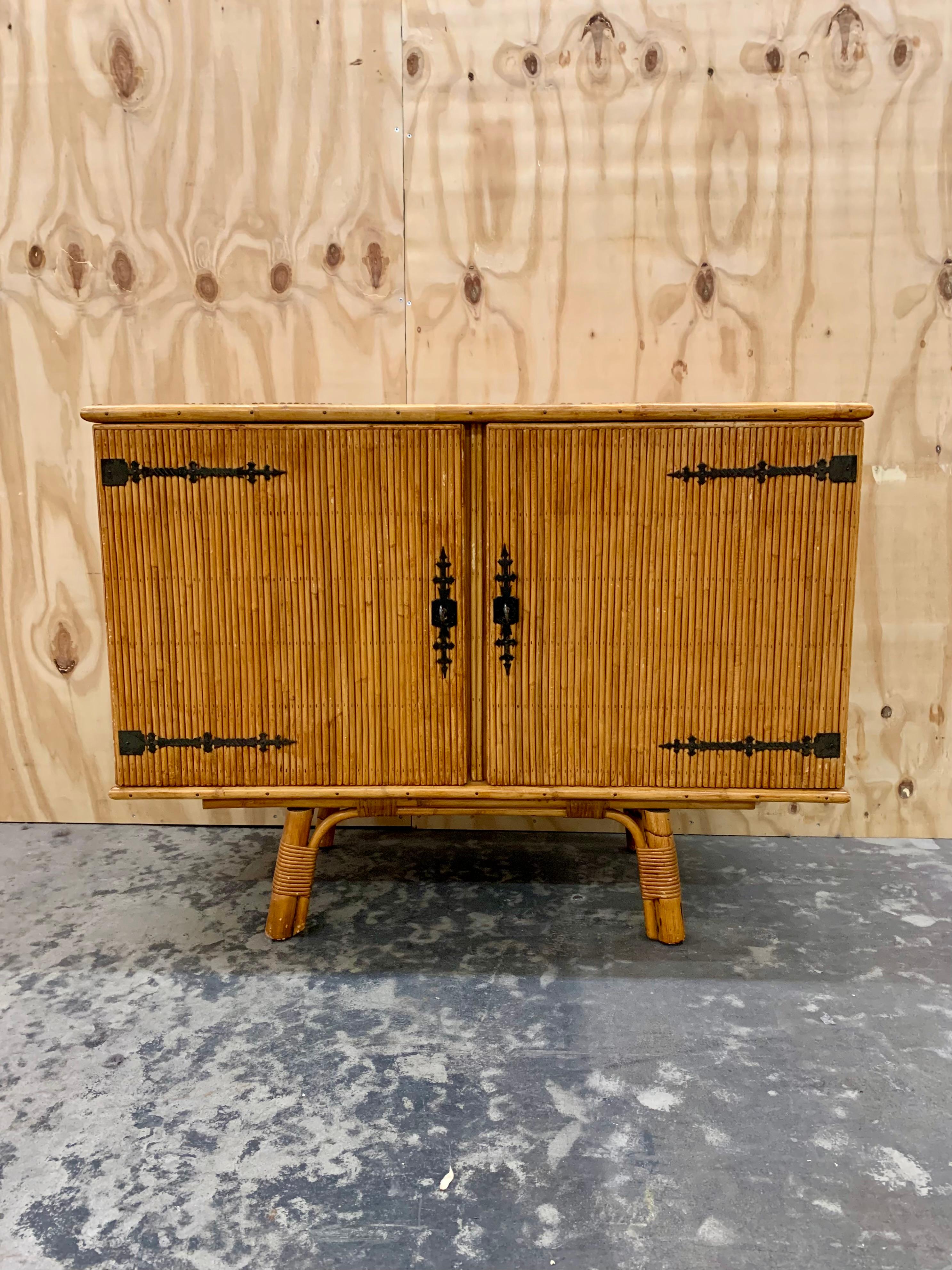 Vintage French bamboo and rattan credenza/sideboard. Hidden behind the 2 doors are 2 shelves. The 1960s Colonial Style bamboo credenza has cool black wrought iron brackets, is in very good condition and will add great ambiance to any home.