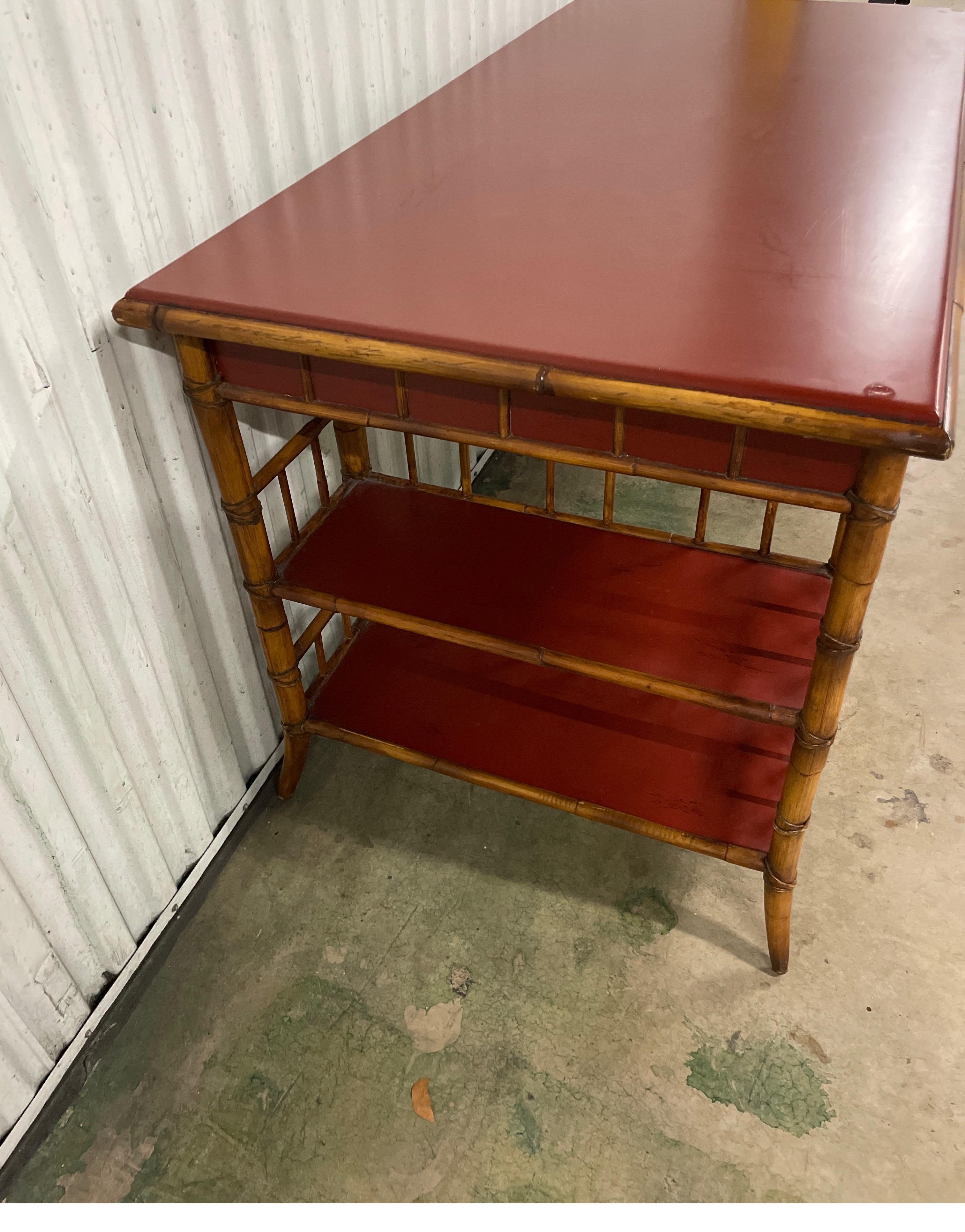 Wonderful Chinoiserie style bamboo desk with red lacquer top for Milling Road by Baker Furniture Company. One large middle drawer which will accommodate your computer. Each side has two shelves for storage.