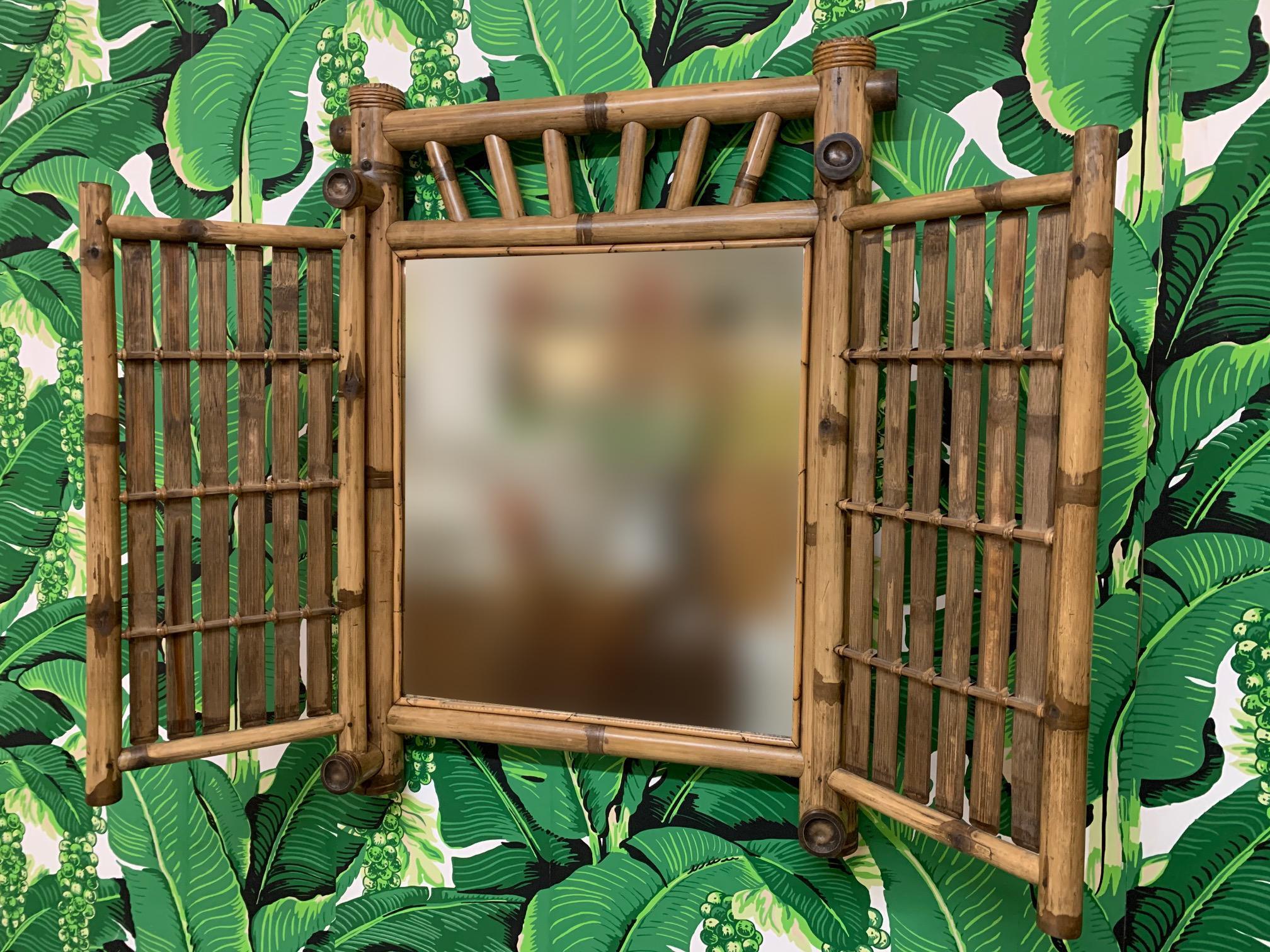 Ce miroir en bambou et rotin de style Tiki est doté d'une double porte qui peut se refermer pour cacher le miroir. Le miroir peut être fixé au mur ou posé sur une commode ou un bureau comme miroir de courtoisie. Une façon parfaite d'ajouter un peu