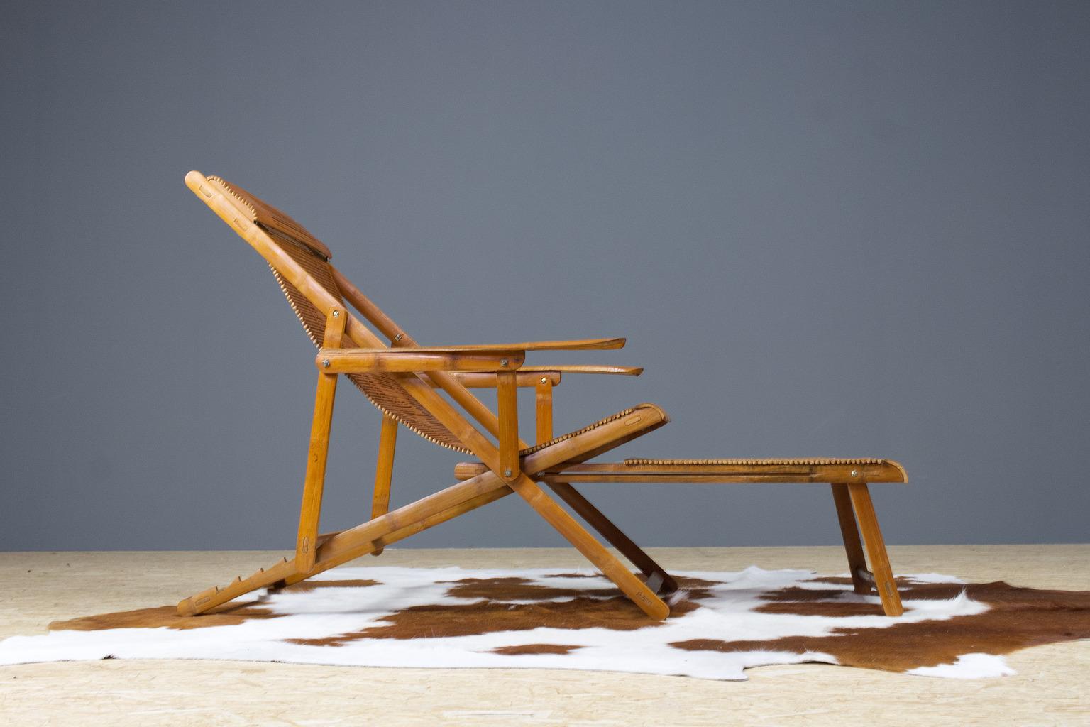A Japanese vintage (1940s) bamboo deck chair with armrest and attached hocker. This handmade lounger is foldable, and has 4 positions. The hocker slides underneath the chair. Honey, warm brown colored bamboo. Incredible great piece of craftsmanship.