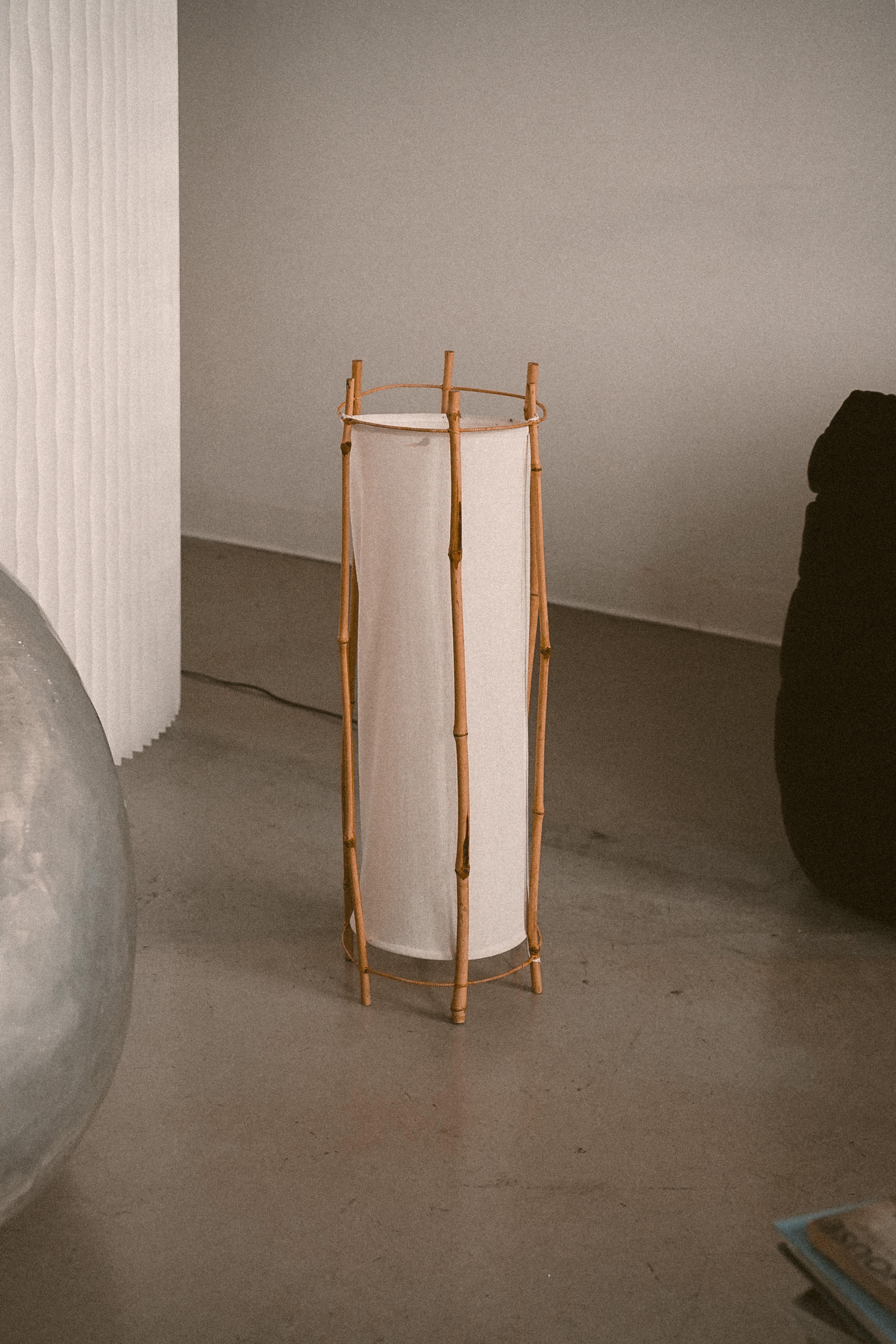 Cylindrical floor lamp in white cotton featuring structure in bamboo composed of six stems. Attributed to the French designer Louis Sognot. Coloured drops of staining on the inside of fabric on one side of the lamp shade, not shown in photos. Please