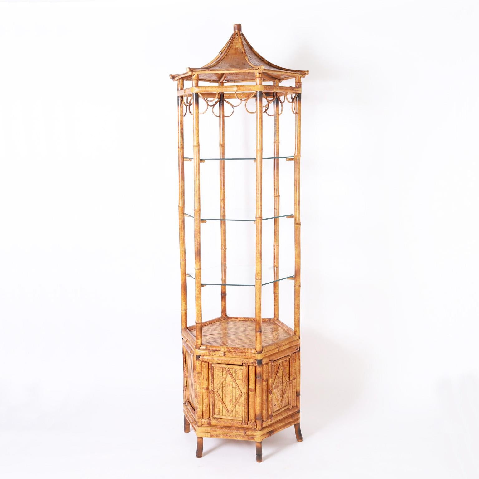 Chic midcentury etagere crafted in bamboo with a woven bamboo pagoda form bonnet over hexagon glass shelves on a bamboo case with a cabinet door and splayed legs.