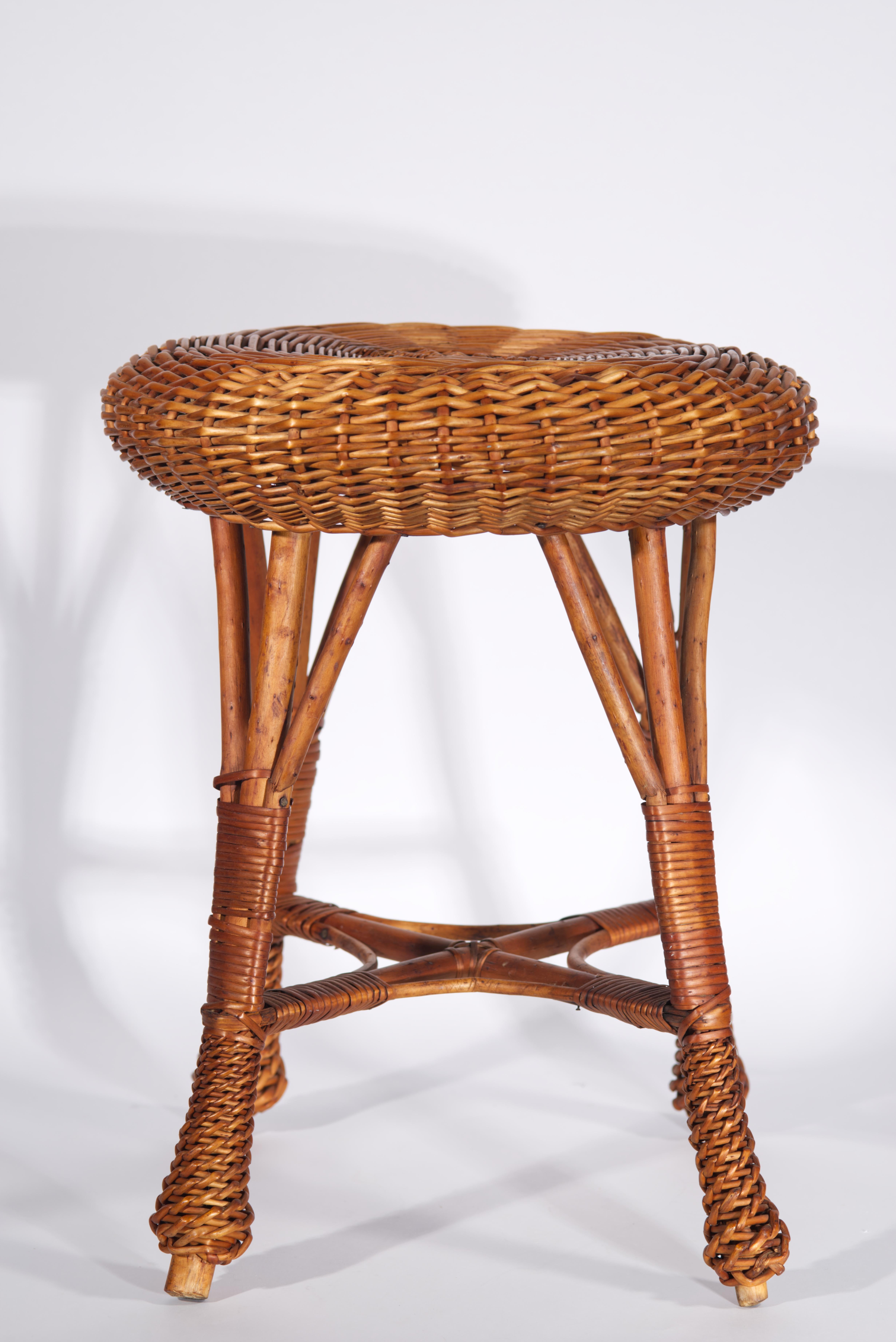 Vintage wicker bamboo stool features a traditional Mid Century Modern silhouette with round woven seat and wide stable legs connected for additional stability by crossing bamboo elements and wrapped in decorative manner in lower half of the legs.