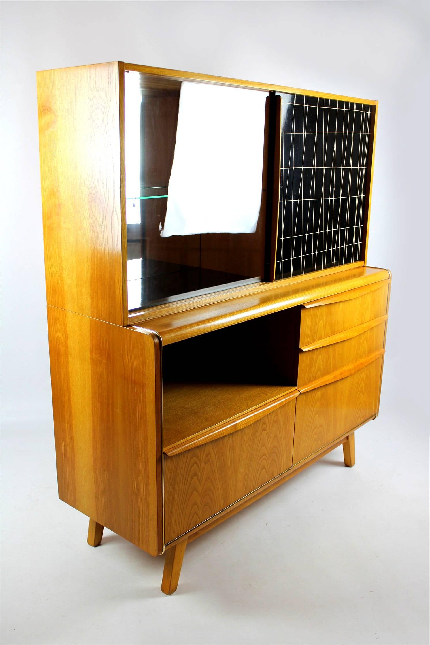 This bar cabinet from the 1960s was designed by Bohumil Landsman for Jitona. It features a thick glass top, two plastic drawers, sliding doors (one with the hand-painted pattern), and a bar cabinet. It is in original condition.