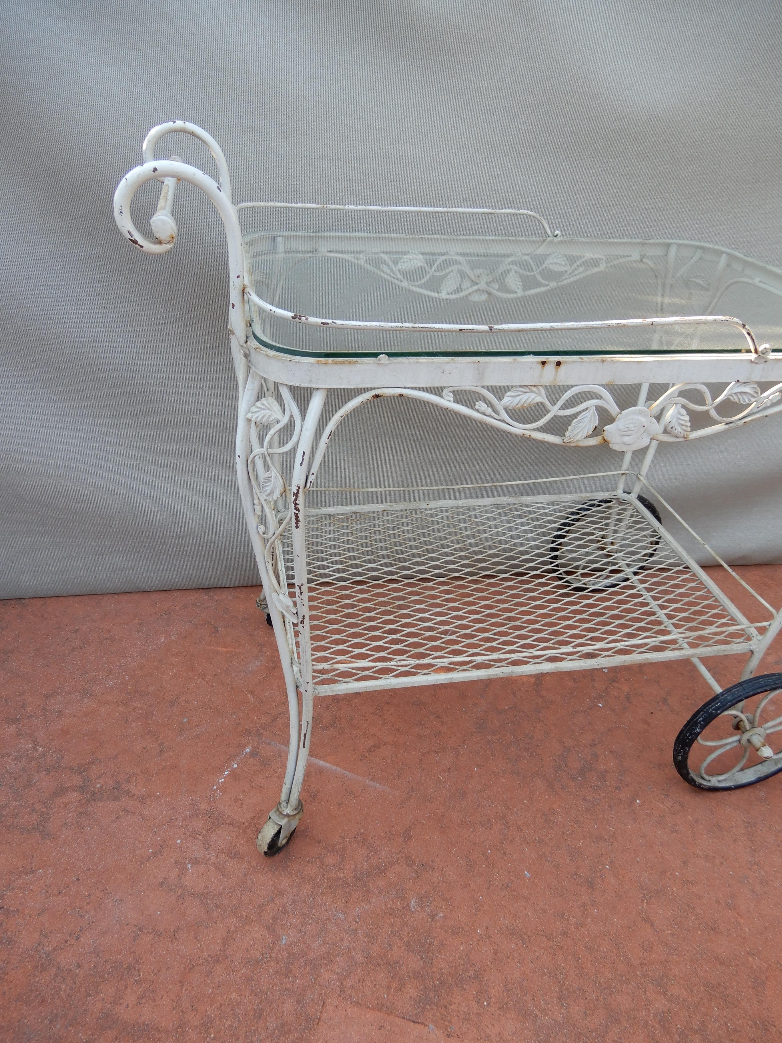 A vintage Woodard tea or bar cart. This wrought iron tea cart was manufactured by the Woodard Company in Michigan. It is in the desirable Chantilly rose pattern. The vintage tea cart maintains an old worn white finish and the original rubber tires