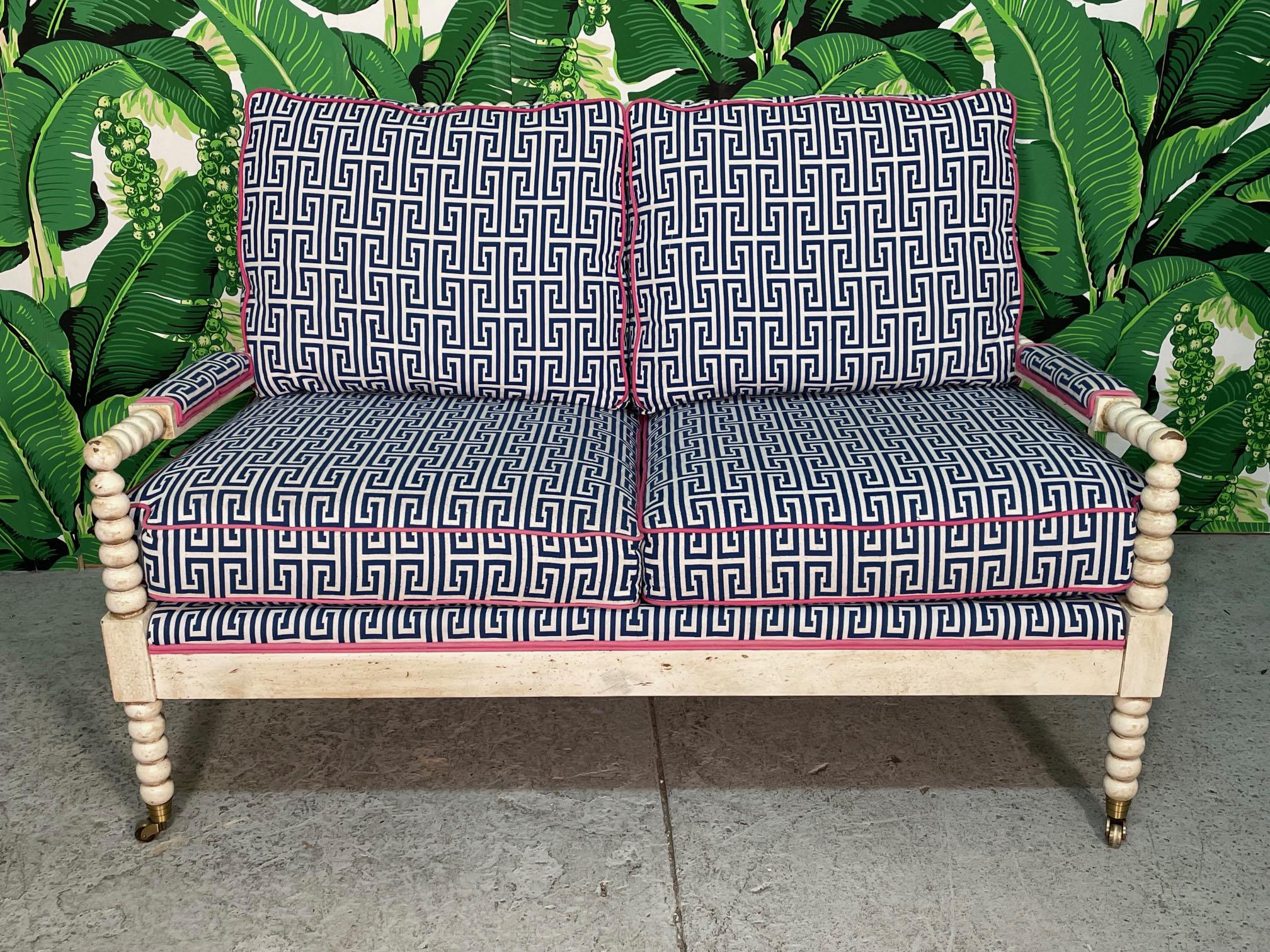 Vintage loveseat features bobbin style frame with colorful upholstery in a greek key print with contrasting welting and brass front roller feet. Excellent structural condition, deep comfortable cushions. Imperfections to frame finish and very slight