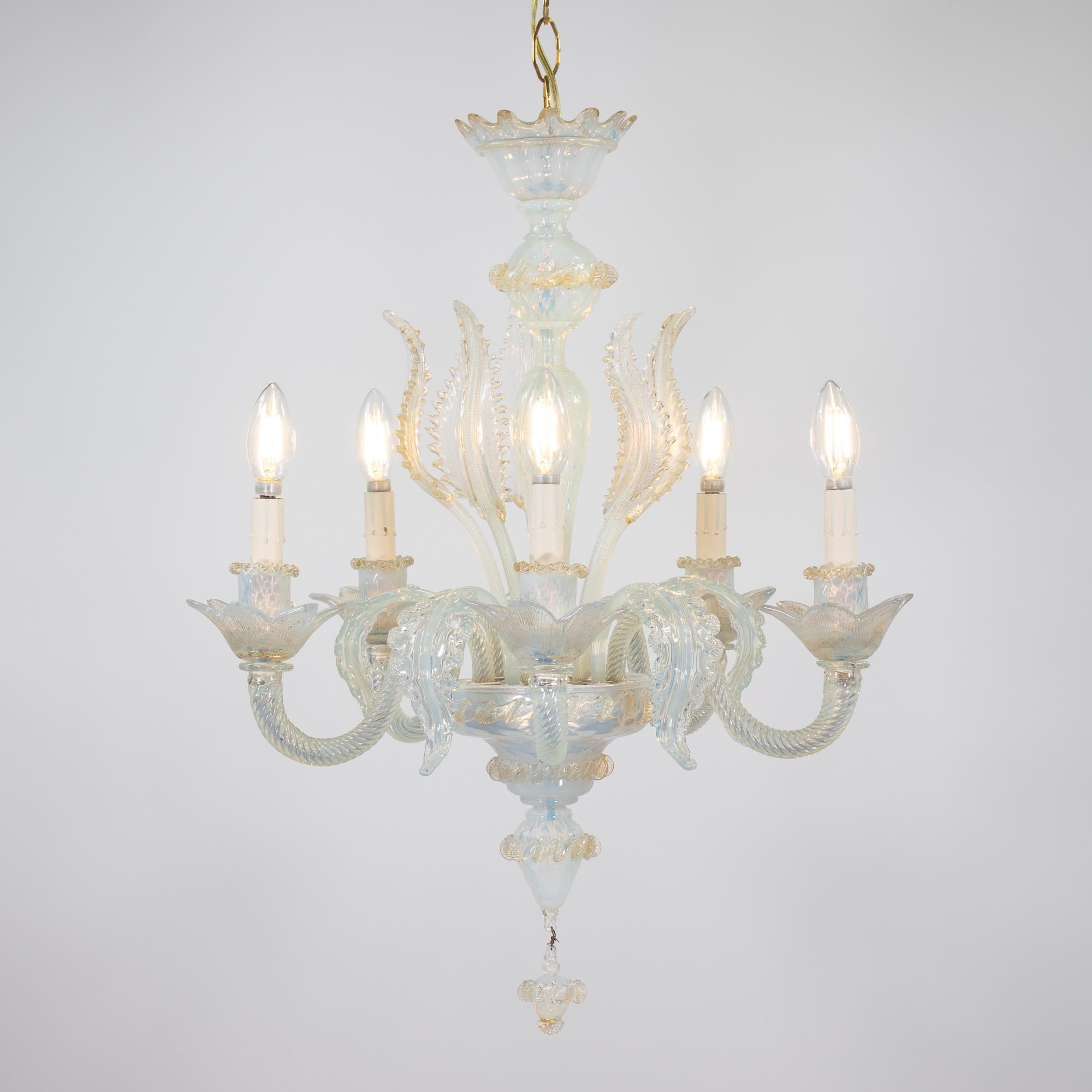 Questo lampadario vintage di Murano in stile barocco, realizzato a mano in oro opalino, ha cinque bracci con bobeches ornate di foglie. Il vetro opalino lattiginoso vira verso un colore azzurro con sottili variazioni di luce. Fiori e foglie