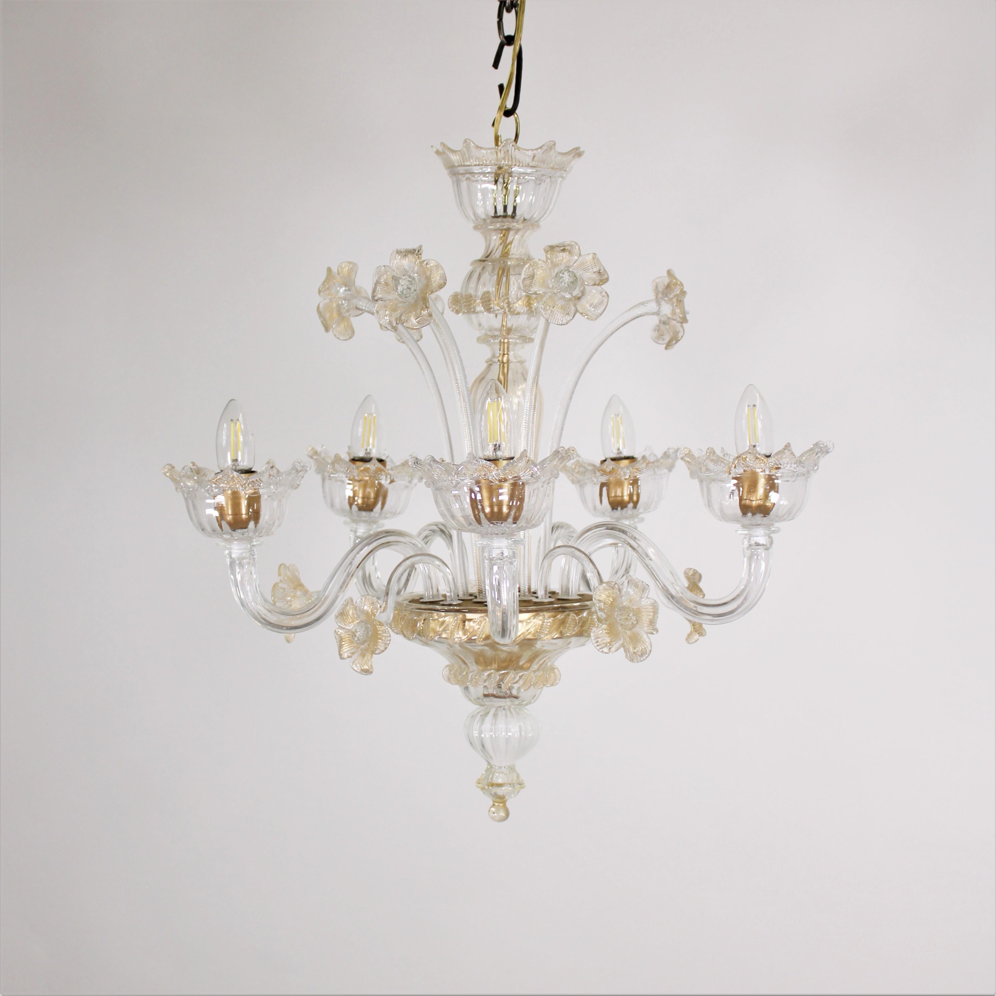 This handcrafted gold-infused cristallo Murano chandelier has five arms holding bobeches with petal-shaped trim and a bulbous center column with rigaree trim. The golden details are concentrated on the flowers and trim details, bringing attention to