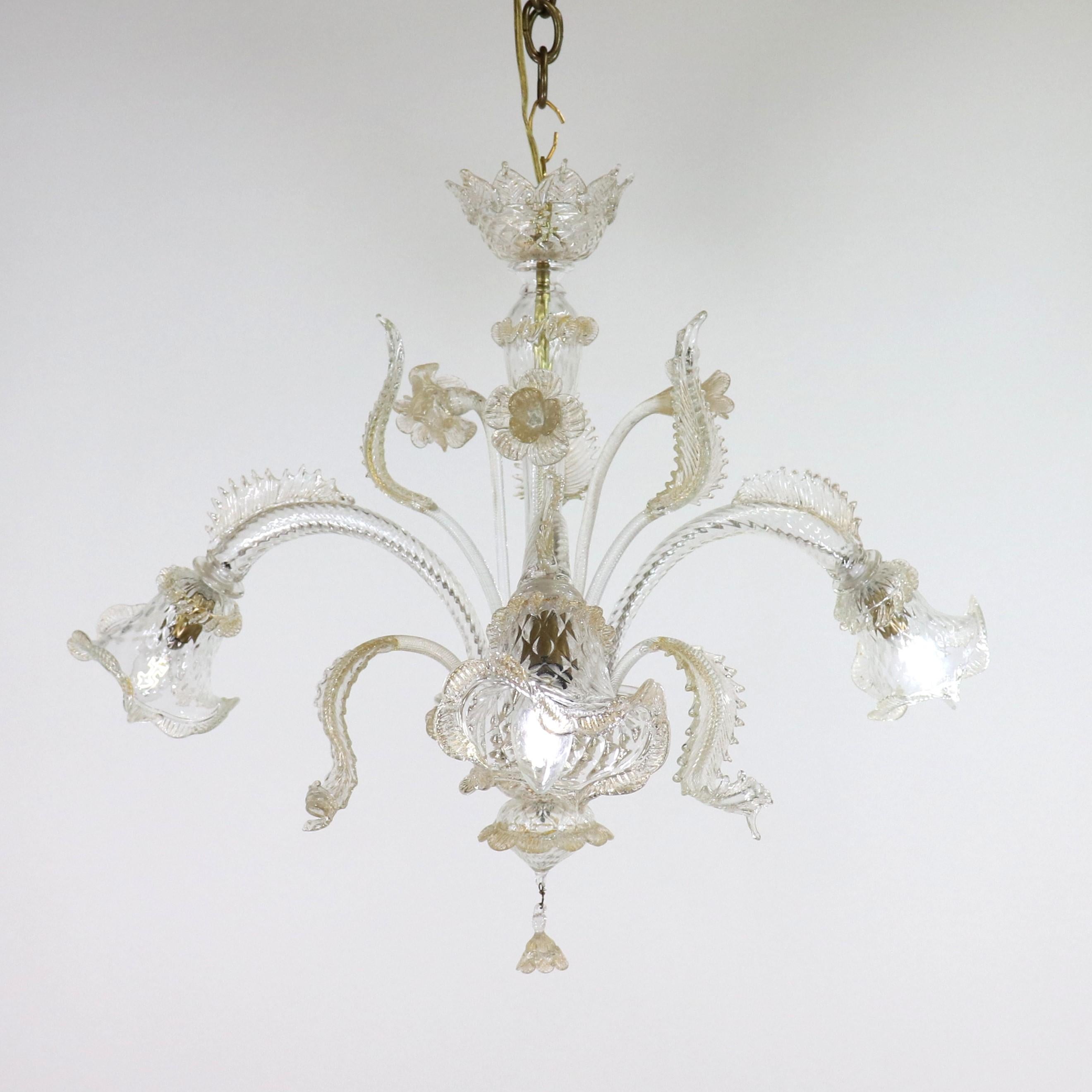 This exquisite, small handcrafted Murano chandelier features gold-infused cristallo glass, adding a touch of elegance to any space. It boasts three gracefully curved scroll arms, each culminating in tri-lobed cups. The timeless Baroque-style floral