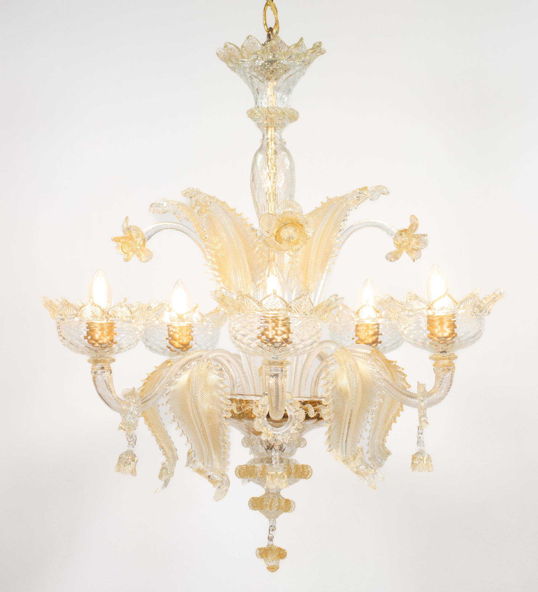Questo lampadario vintage in stile barocco in Cristallo di Murano infuso d'oro è caratterizzato da cinque bracci a voluta con coppe ornate di petali, da cui pendono baubles ad anello con fiocchi penzolanti. Il centro è decorato con una serie di