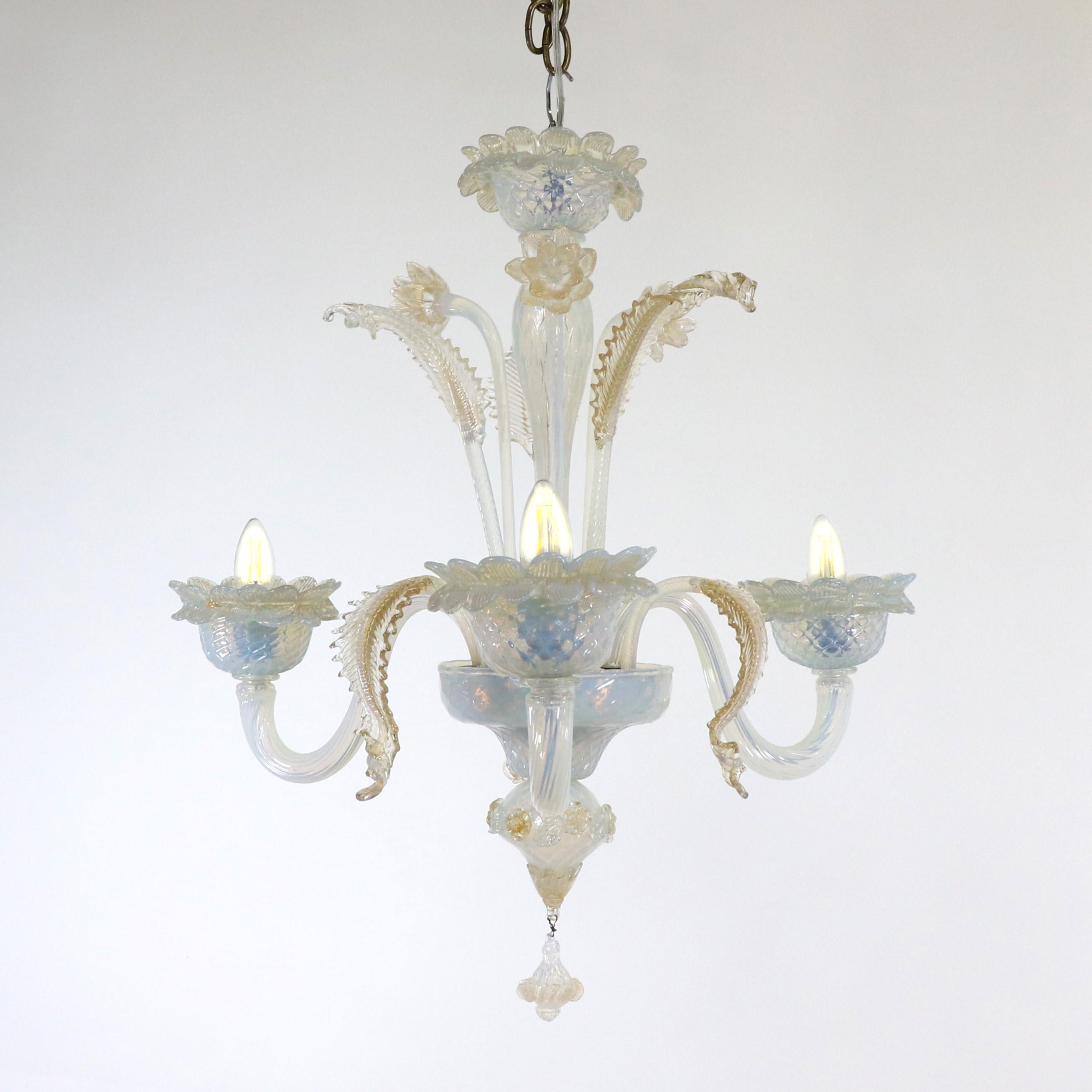Questo lampadario opalino di Murano, squisitamente realizzato a mano, è dotato di tre bracci flessuosi con coppe ornate di petali. Il vetro opalino lattiginoso vira verso un colore azzurro con sottili variazioni di luce. Fiori e foglie abbelliscono