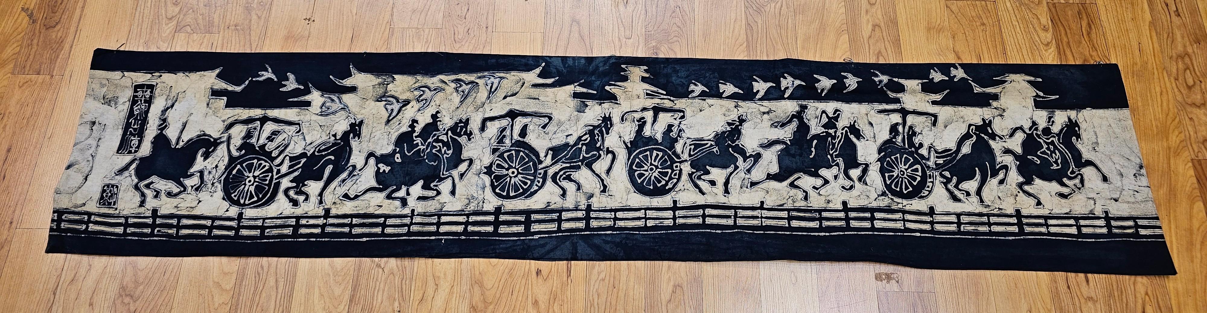 Batik asiático vintage pintado a mano.  El hermoso batik es una representación panorámica de jinetes en carros y a caballo sobre una tela de color índigo con diseños en marfil.  El batik es un maravilloso ejemplo de arte mural pintado a mano.   
El