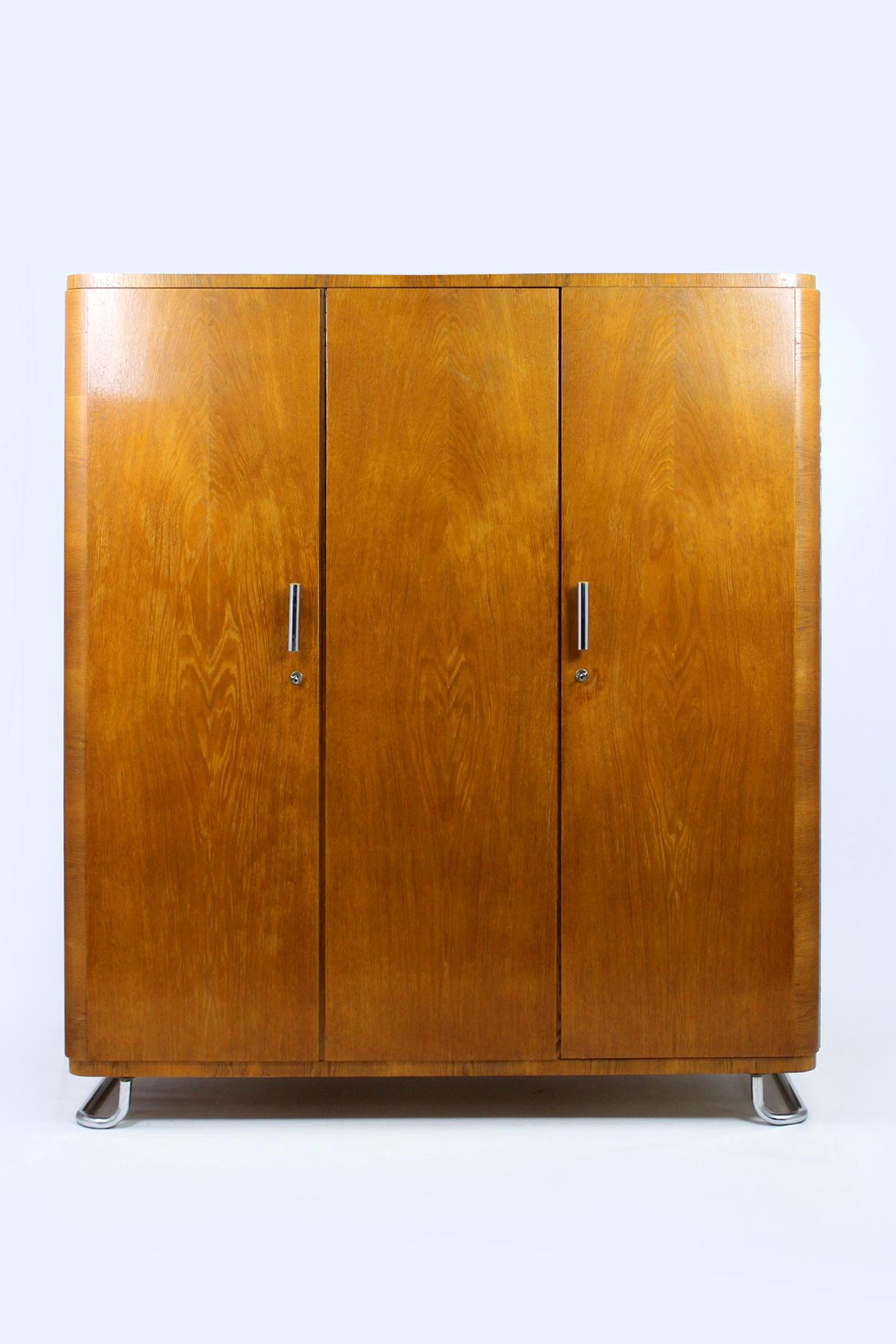 Cette armoire de style Bauhaus a été produite par Hynek Gottwald en Tchécoslovaquie dans les années 1930. Elle est dotée de trois portes, d'un portemanteau intérieur et de cinq étagères. L'armoire repose sur des pieds chromés et possède des poignées