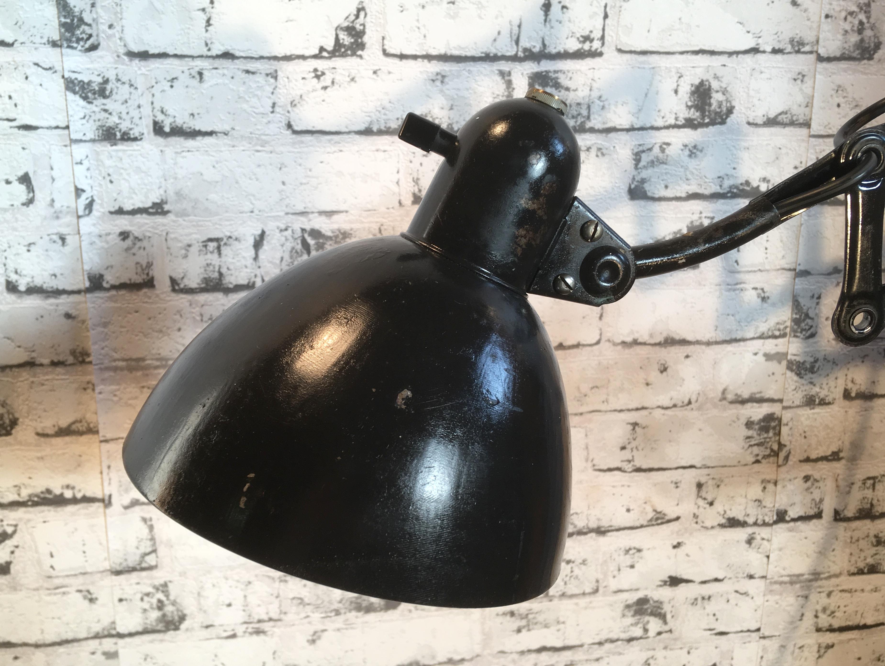 This vintage industrial scissor lamp in Bauhaus style was produced during the 1930s. The lamp has a black metal shade, white interior. Black iron scissor arm is extendable and can be turned sideways. Original socket for E 27 bulbs with rotary