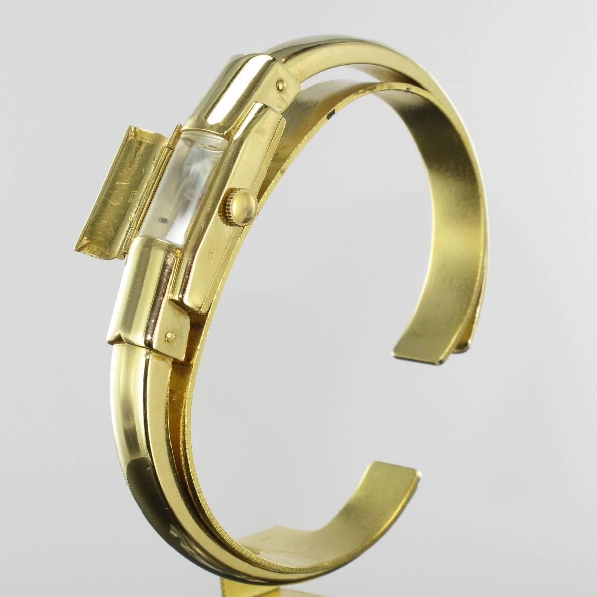 Montre pour femme Baume & Mercier.
Boîtier rectangulaire en or jaune 18 carats, poinçon tête d'aigle, dissimulé sous une plaque d'or rectangulaire convexe.
Montre mécanique à remontage manuel.
Fond blanc.
Bague ovale en or jaune, 18 carats, avec
