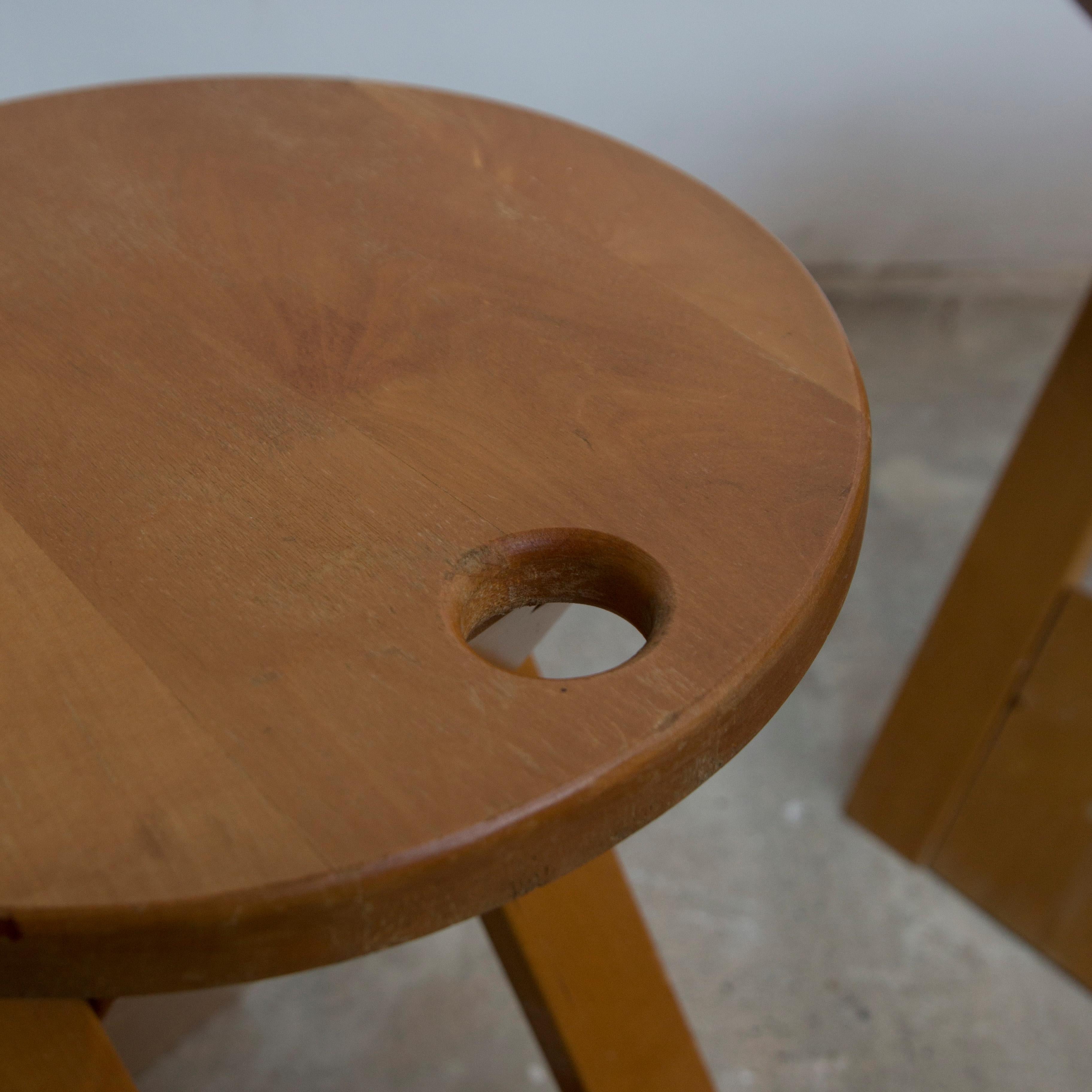 This pine stool from the 1980s has a minimalist design. Designed by Adrian Reed for Princes Design works Limited in London in 1984. It is foldable and has a hole allowing its suspension for optimal space saving. It is made of solid pine, foldable