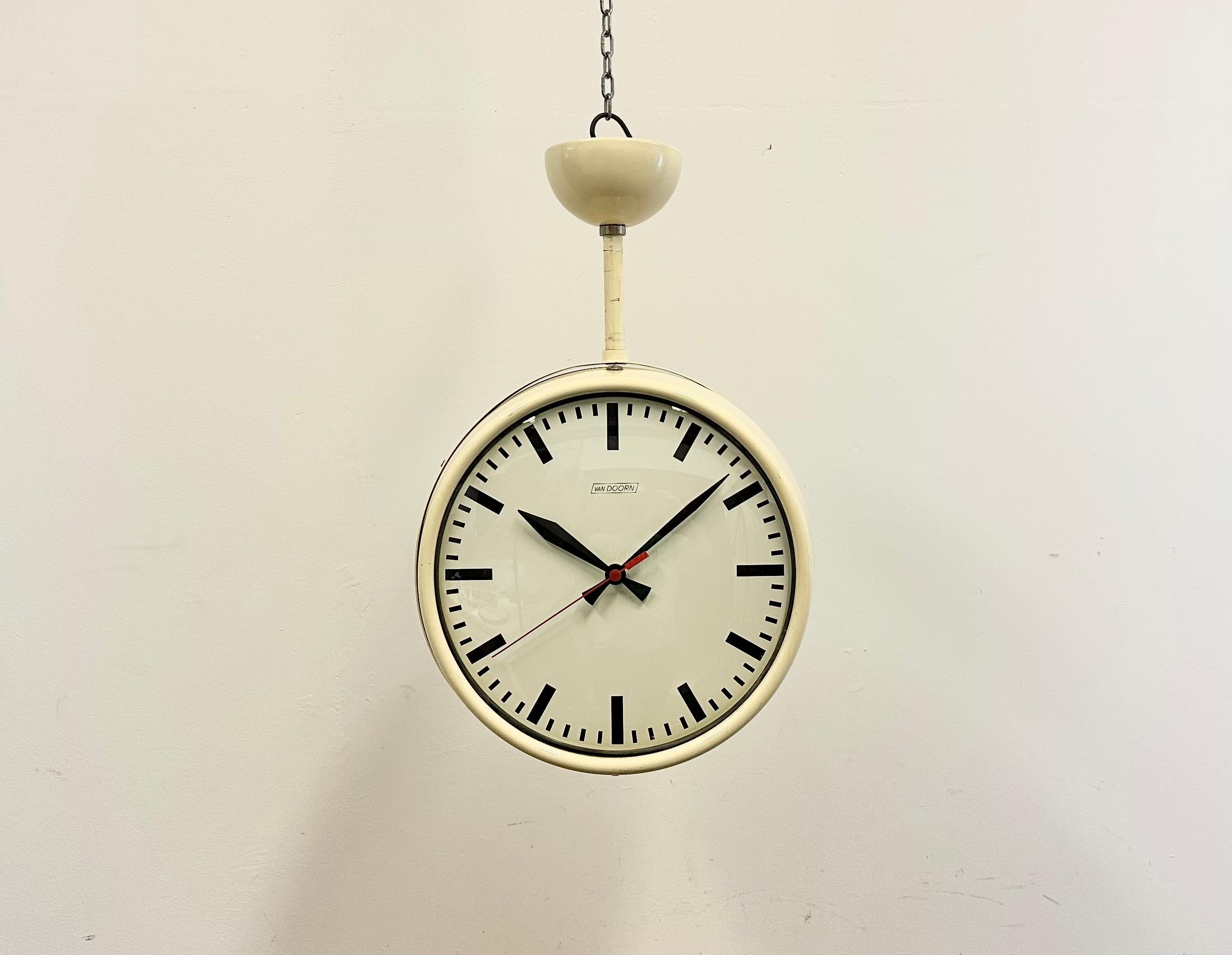 This double sided hanging ceiling clock was produced by Van Doorn in Netherlands during the 1960s. It features a beige iron body, an iron dials, an aluminum hands and a convex clear glass covers. The piece has been converted into a battery-powered