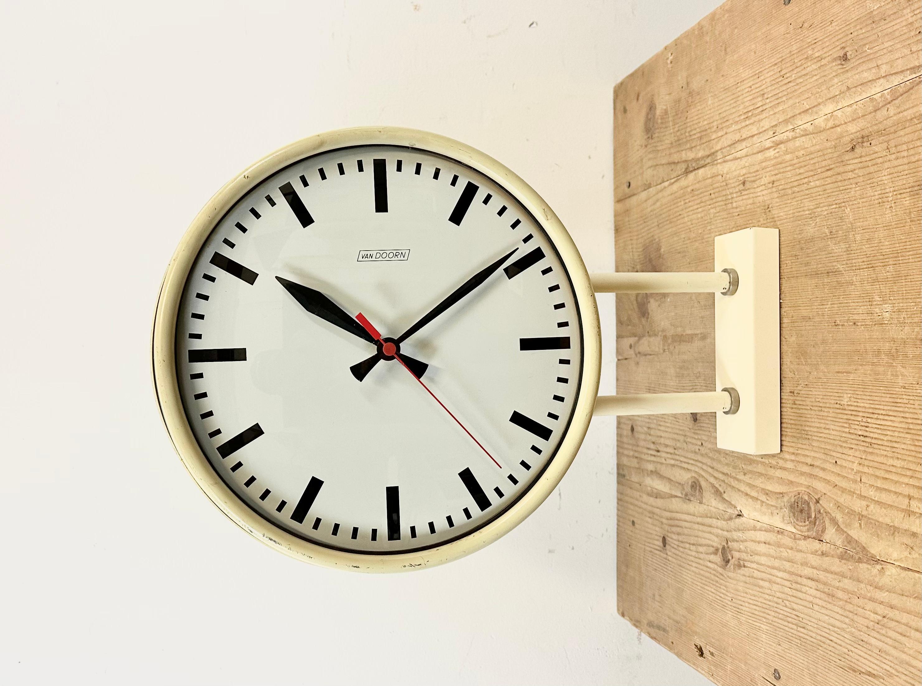 This double sided wall clock was produced by Van Doorn in Netherlands during the 1960s. It features a beige iron body, an iron dials, an aluminum hands and a convex clear glass covers. The piece has been converted into a battery-powered clockwork