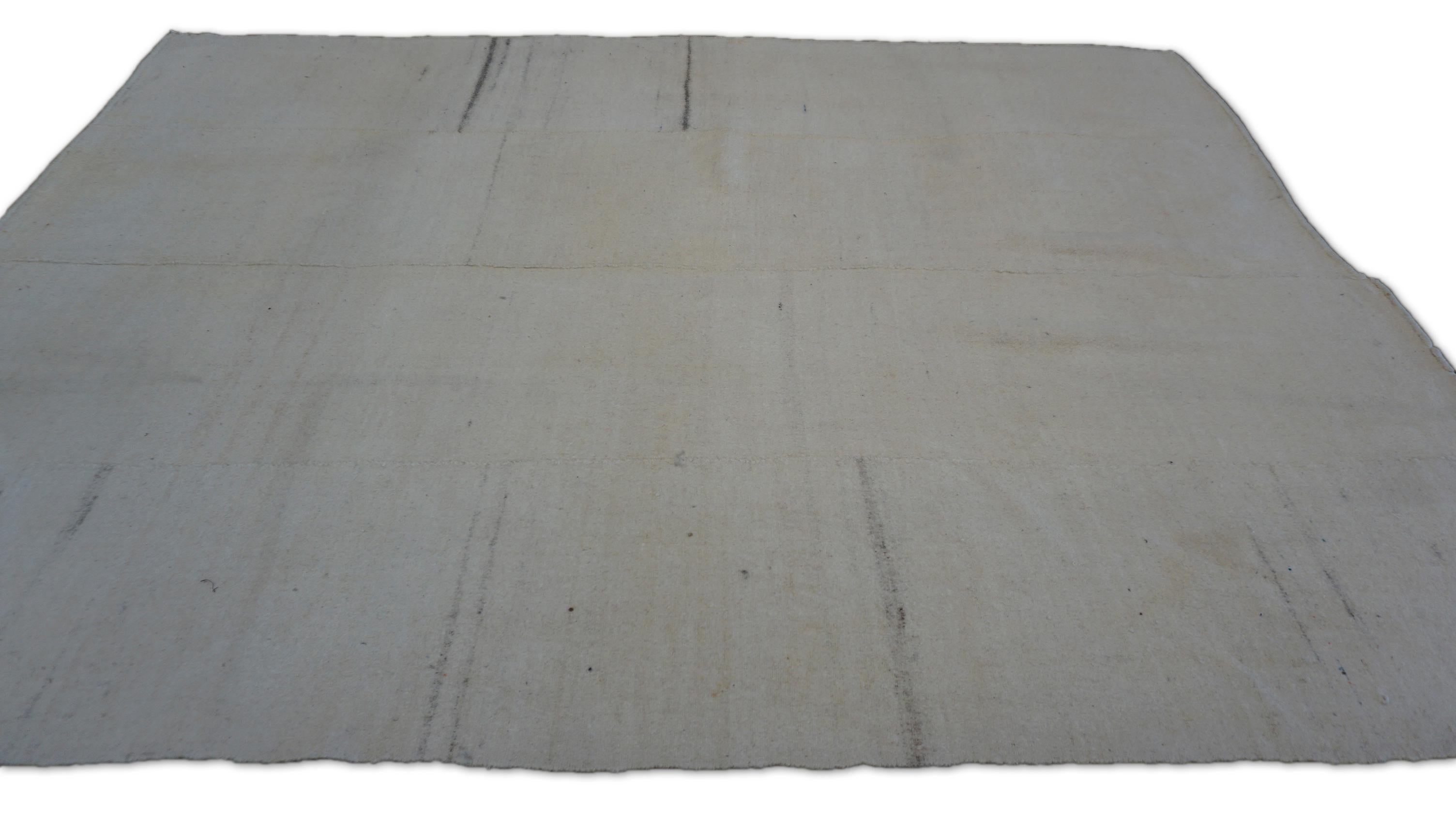 Esta discreta alfombra vintage es una refinada expresión de diseño minimalista y herencia artesanal. Tejida a mano con lana sin teñir, la pieza muestra un sereno campo marfil sutilmente marcado por tenues estrías lineales en suaves variaciones