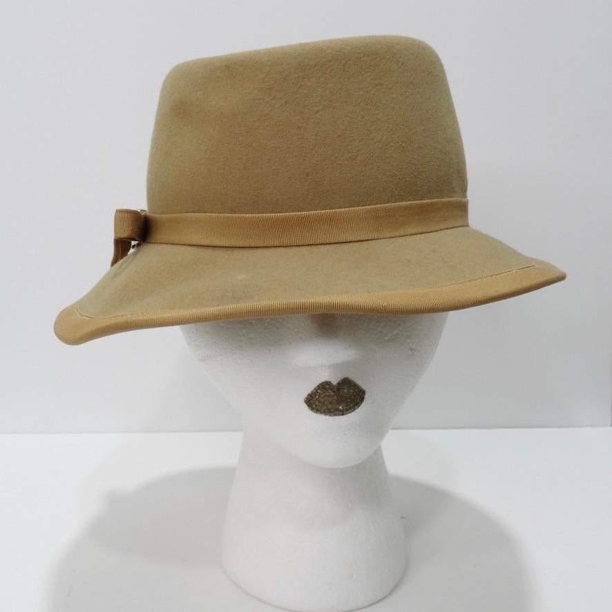 Ce chapeau beige vintage Pierre Cardin est une pièce intemporelle et incontournable. Celui-ci est dans une nuance neutre de marron clair, avec un lien autour du centre, fixé avec du matériel argenté. Ce chapeau est tellement polyvalent qu'il peut