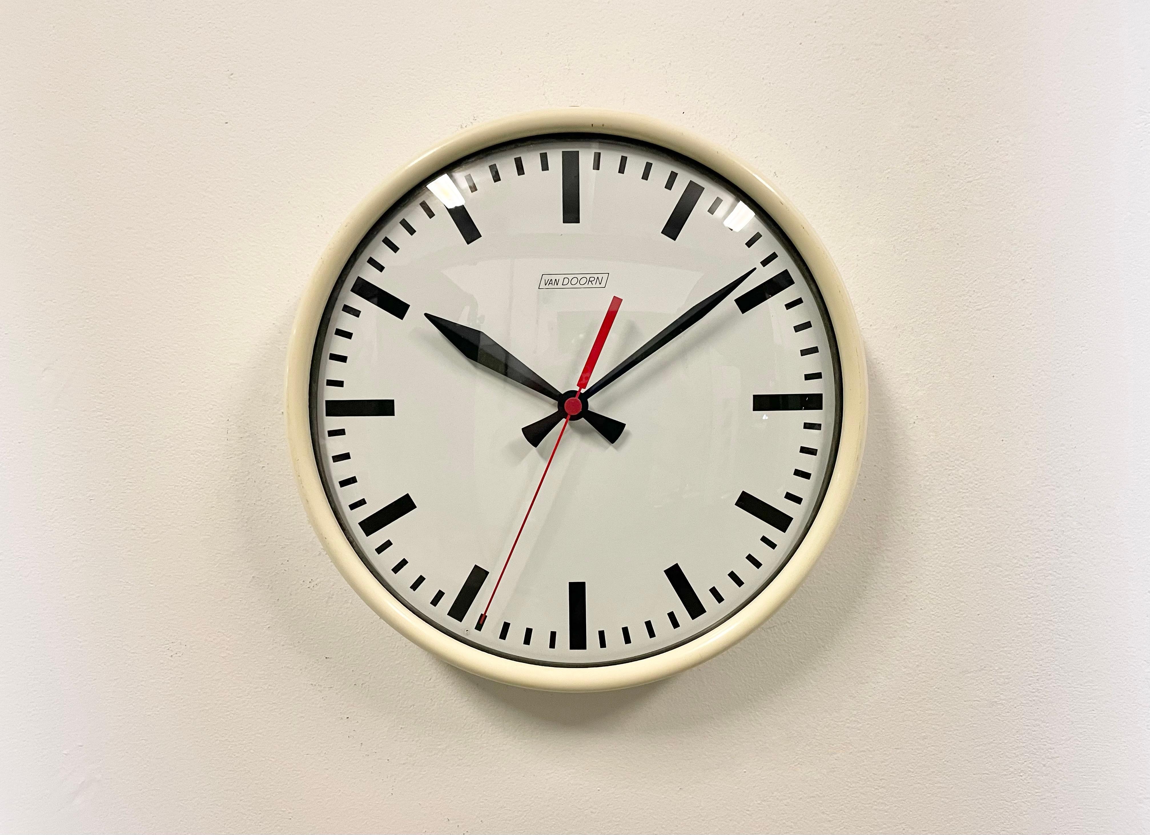 Wall clock produced by Van Doorn in Netherlands during the 1960s. It features a beige iron frame, an iron dial, an aluminum hands and a curved clear glass cover. The piece has been converted into a battery-powered clockwork and requires only one