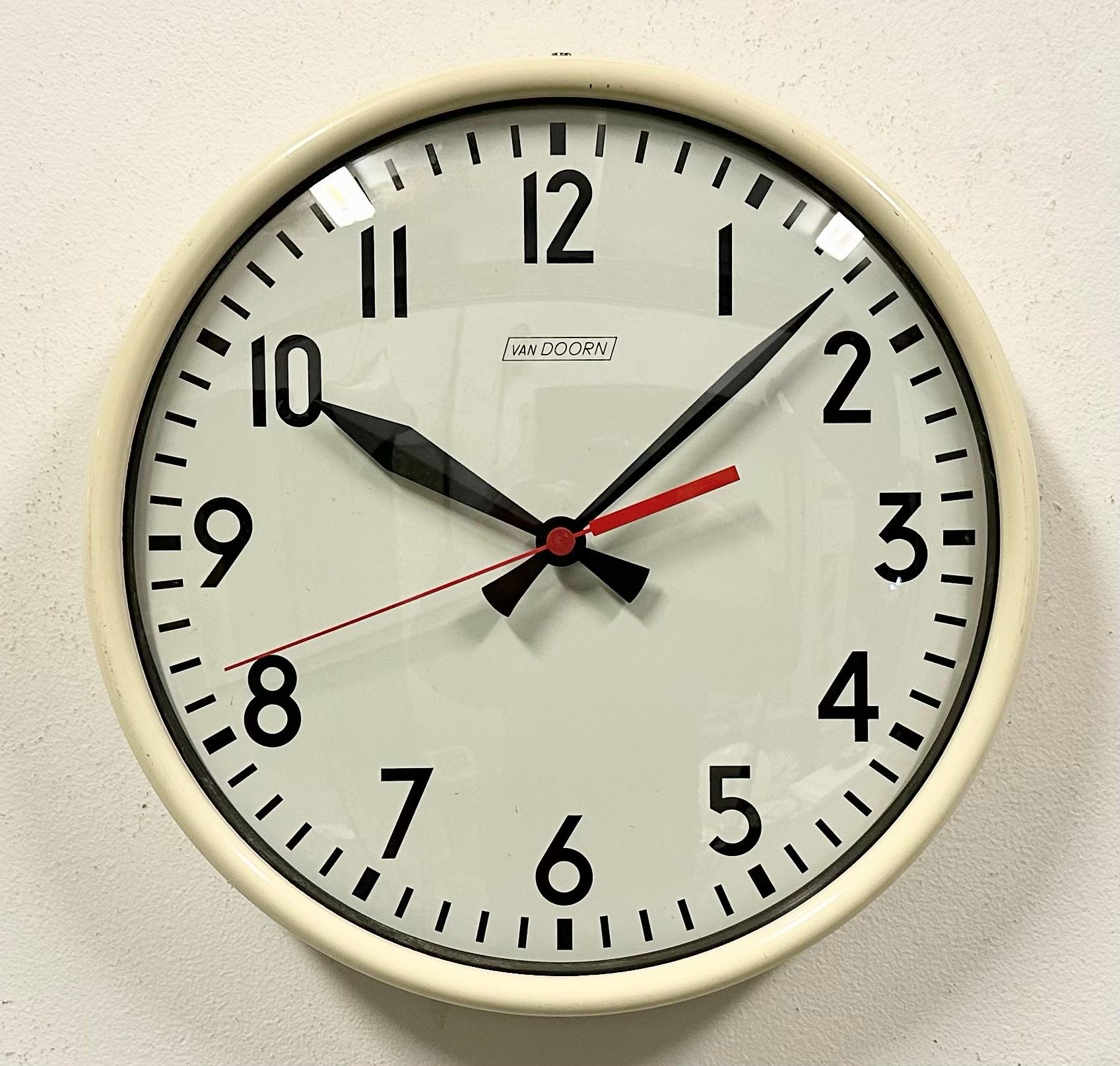 This wall clock was produced by Van Doorn in Netherlands during the 1960s. It features a beige iron frame, an iron dial, an aluminum hands and a curved clear glass cover. The piece has been converted into a battery-powered clockwork and requires