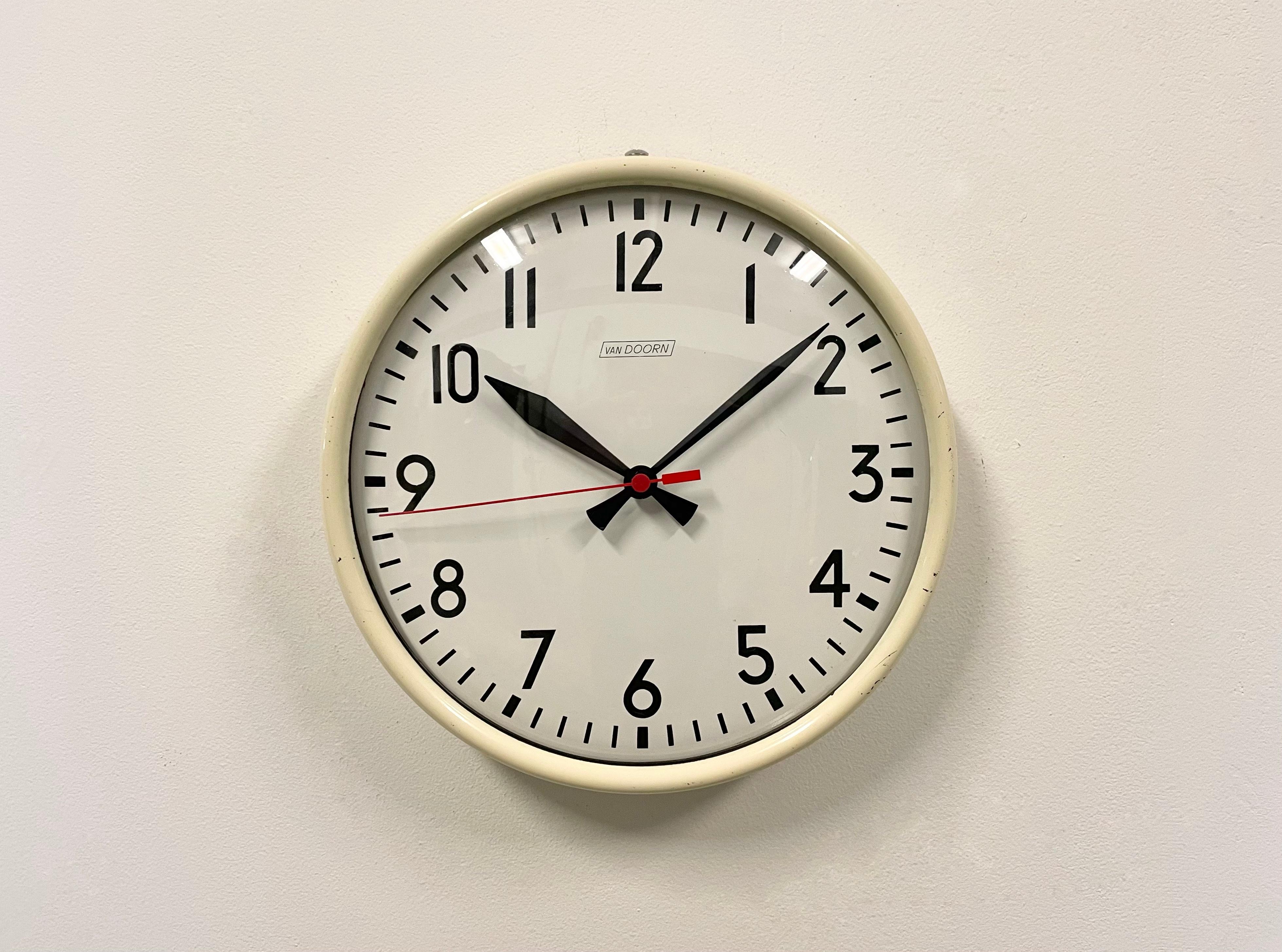 This wall clock was produced by Van Doorn in Netherlands during the 1960s. It features a beige iron frame, an iron dial, an aluminum hands and a curved clear glass cover. The piece has been converted into a battery-powered clockwork and requires