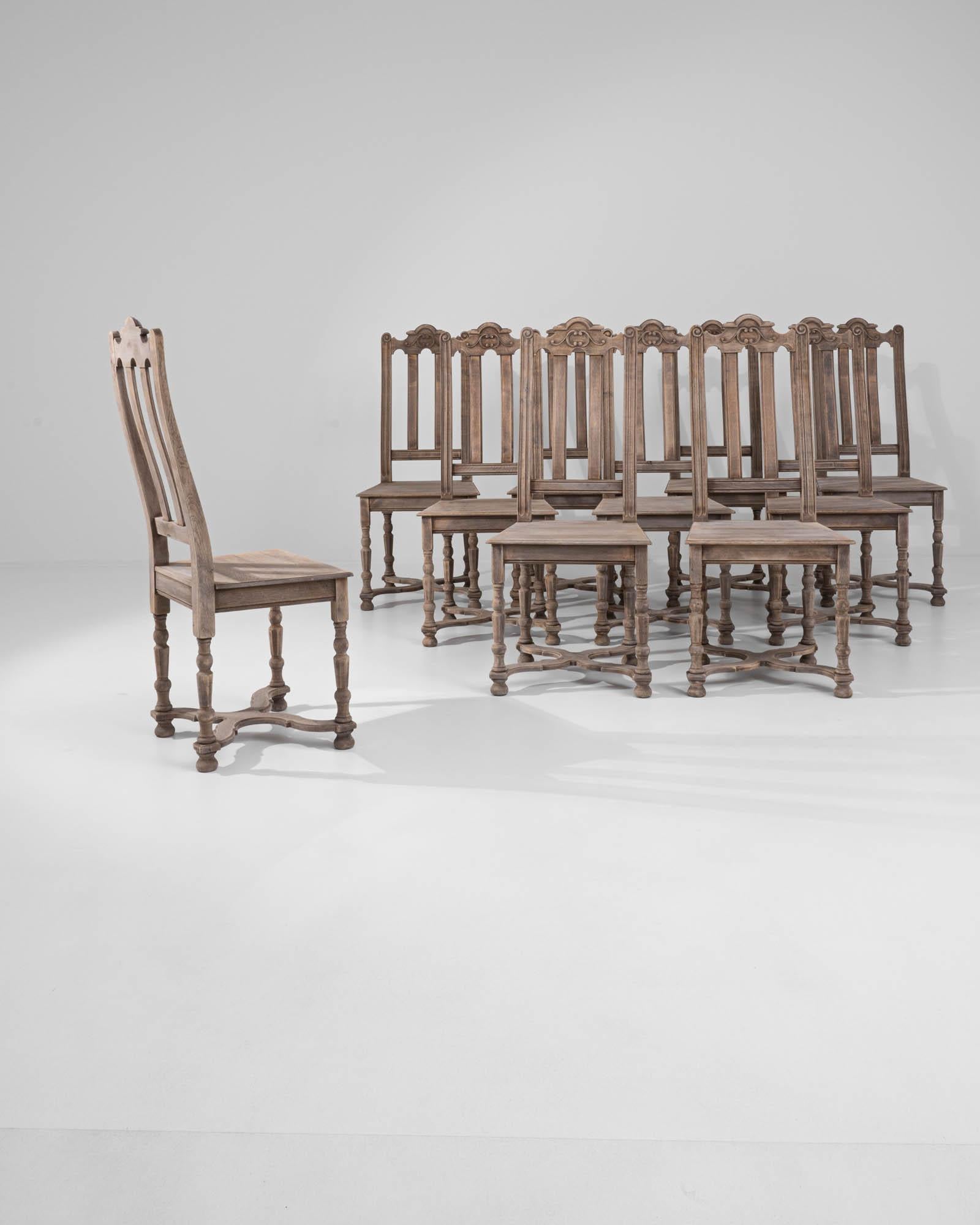 A set of oak dining chairs made in 20th century Belgium. High-backed and composed with impeccable posture, this grouping of ten astute chairs emits a distinguished air of regality. The oak that composes its structure has been treated with a delicate