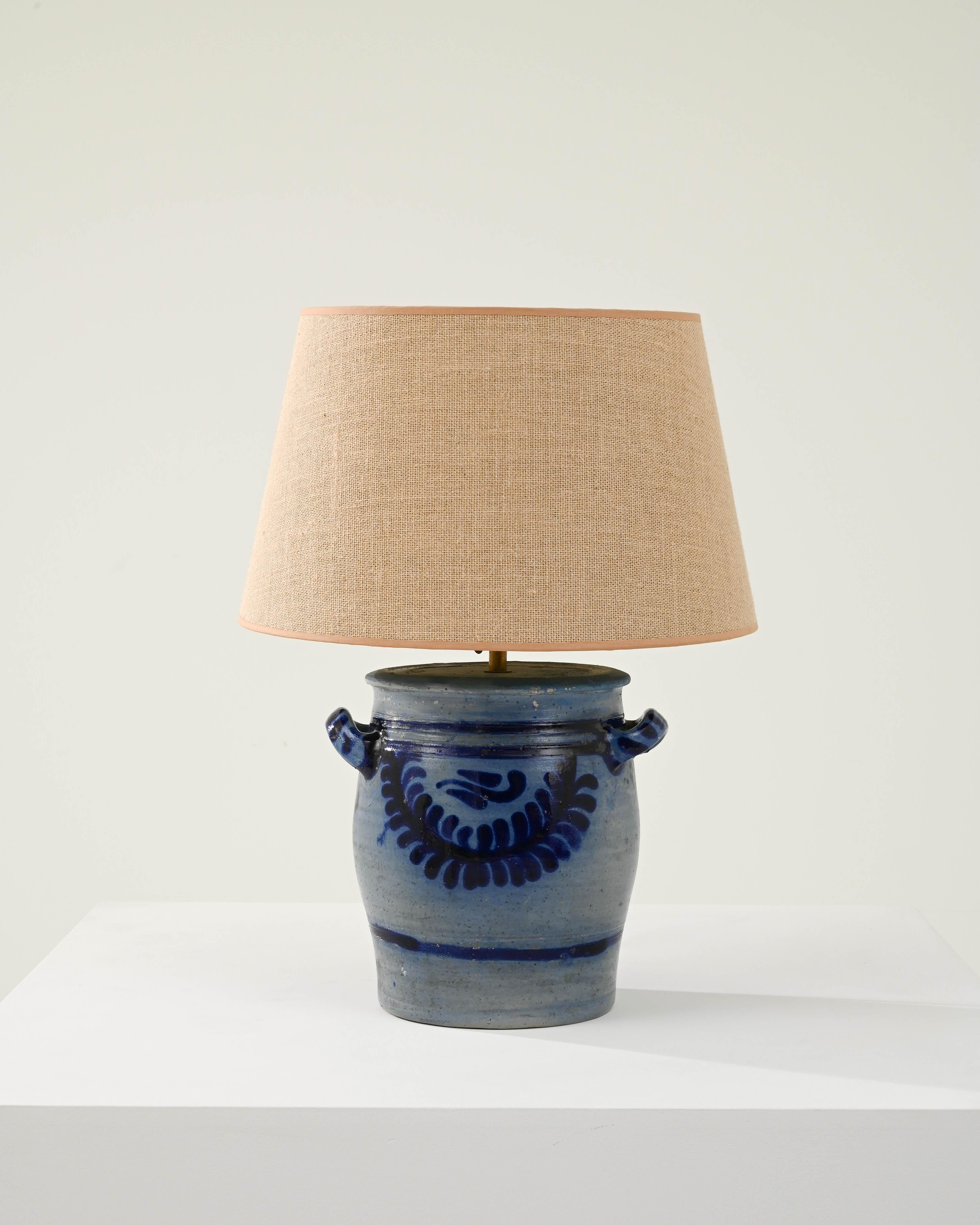 This eclectic-styled ceramic lamp comes from 1900s Belgium. The typical country pot is finished with a vivid blue salt glaze, appealing in its azure palette complemented with warm tones on its empire shade which also contrasts with its rounded clay