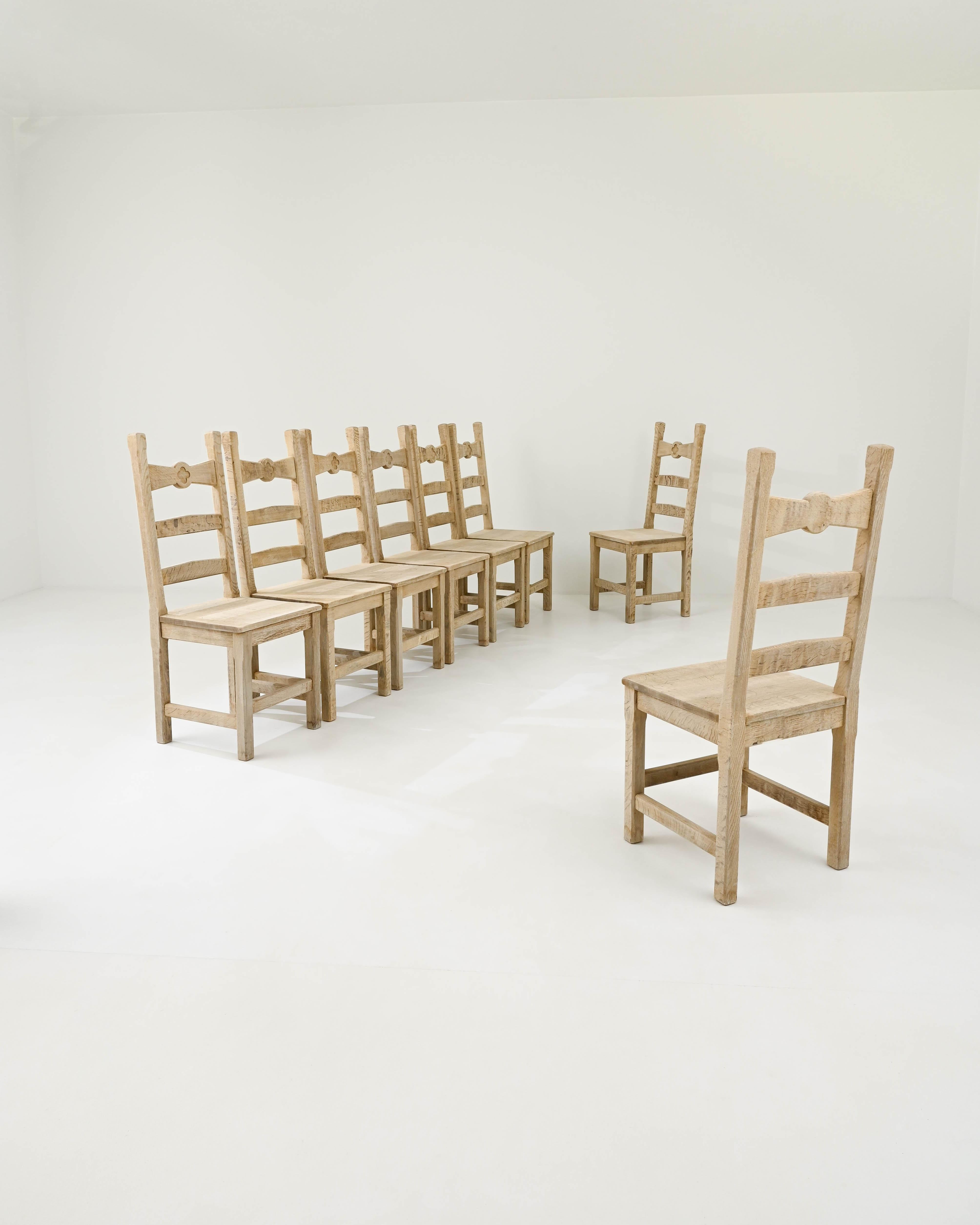 A set of oak dining chairs created in 20th Century Belgium. Silvery brown and mat hardwood composed into a thoughtful and utilitarian construction characterizes these chairs as a farmhouse style staple. Charming dowel rod pegs, carved seat backs,