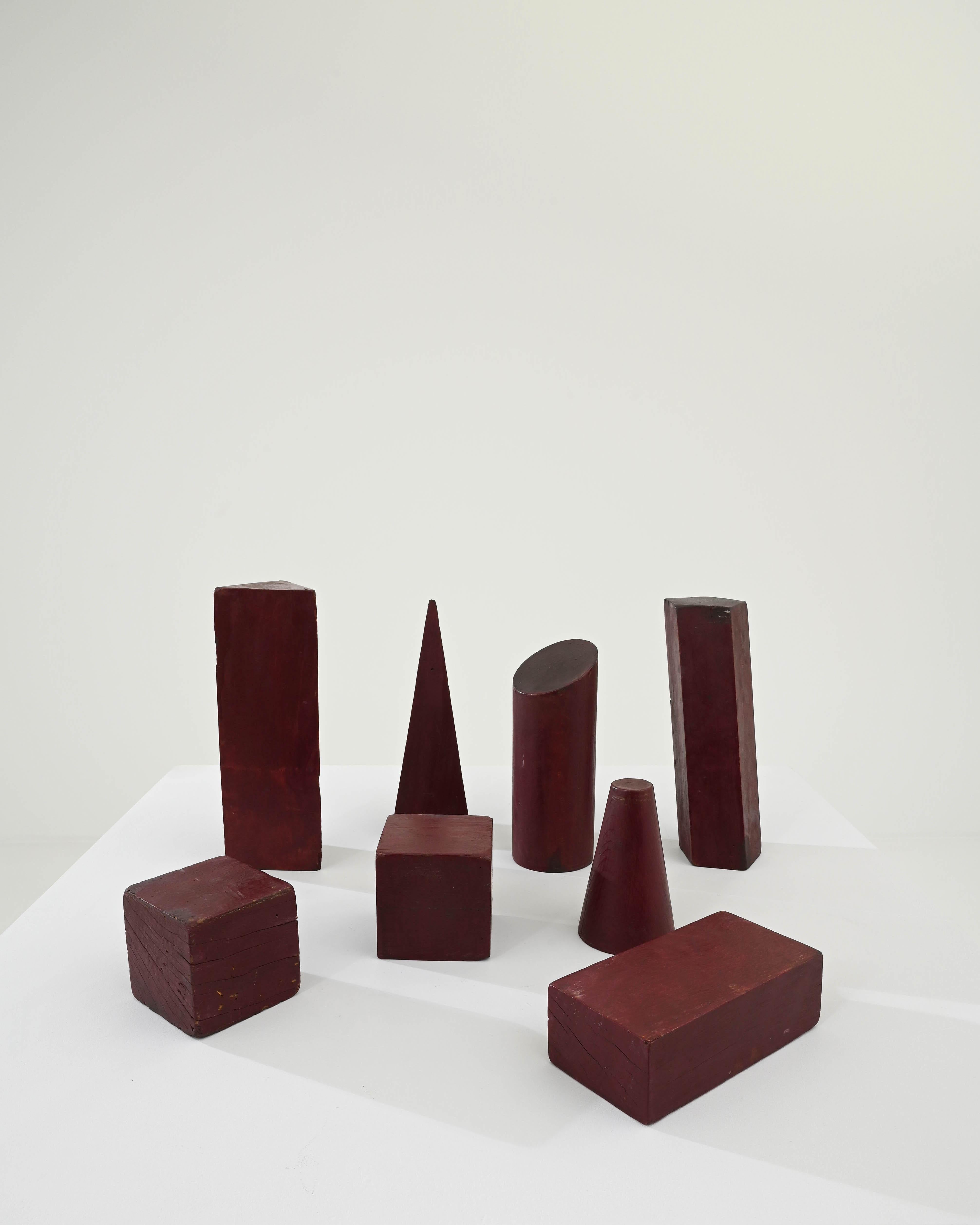 A set of wooden decorations created in 20th century Belgium. A motley cast of characters, these geometric solids gather round, casting overlapping shadows together. Underneath the dark and warm maroon paint one can make out the wood grain below,