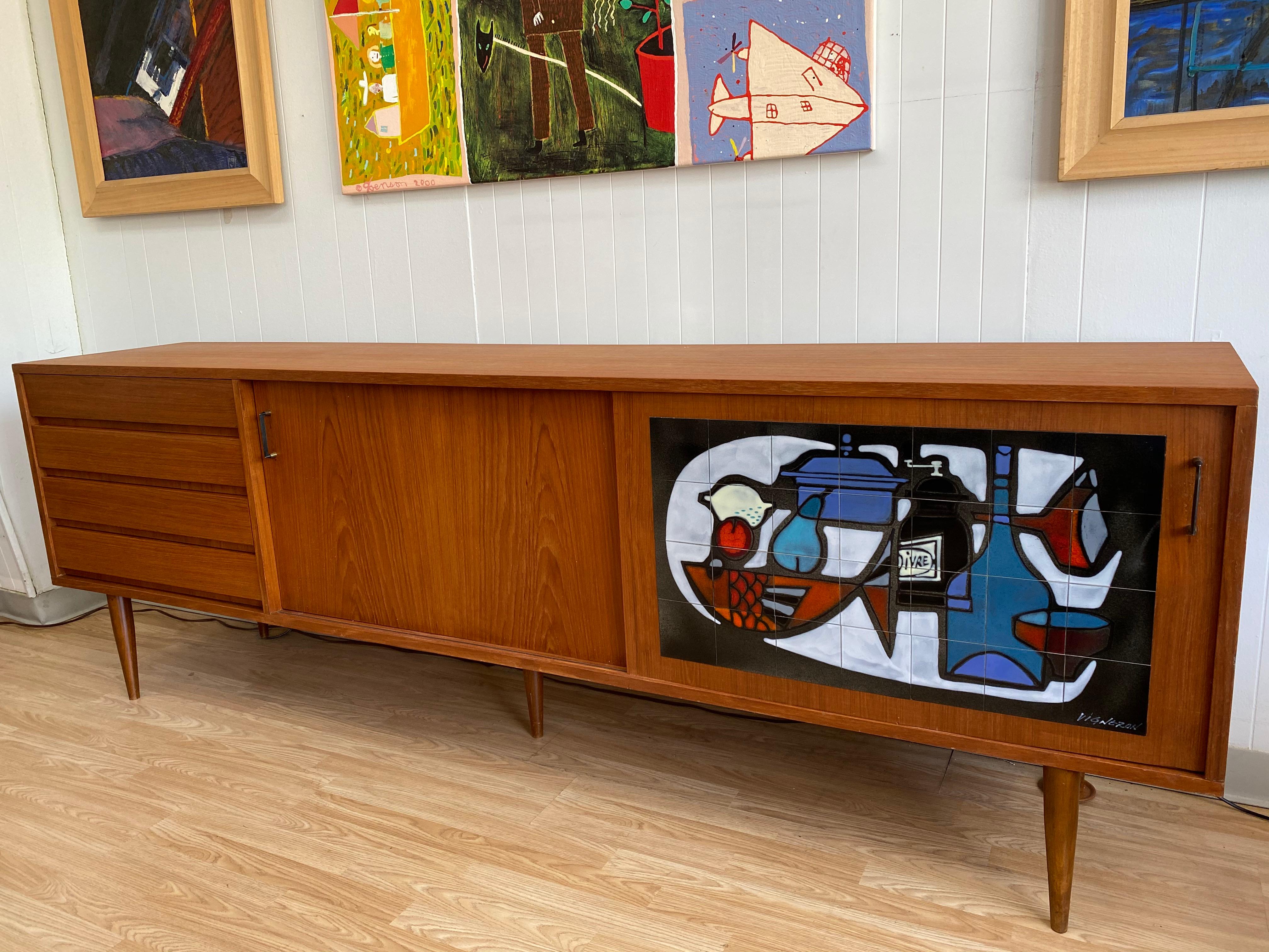 This vintage Belgian modern teak credenza with inlaid enamel on copper tile is in overall very good condition. Two large sliding doors and a set of four drawers. Signed Vigneron,
circa 1960s. Belgium.
Dimensions:
19