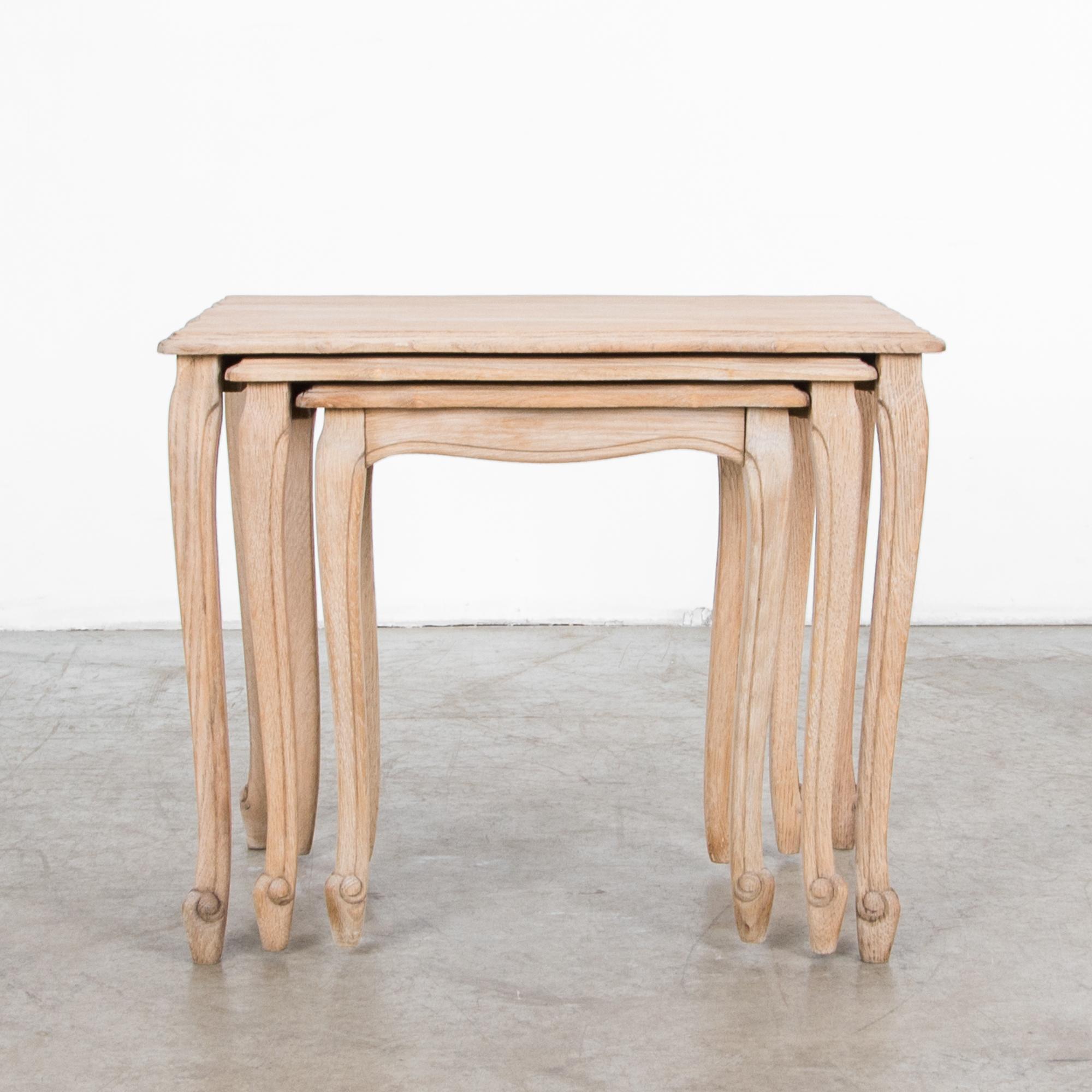 A set of three nesting tables from Belgium, circa 1950. Slender cabriole legs, featuring a subtle scroll, support a tabletop with a scalloped and carved table edge. Made of bleached oak, the understated finish gives these nesting tables a classic