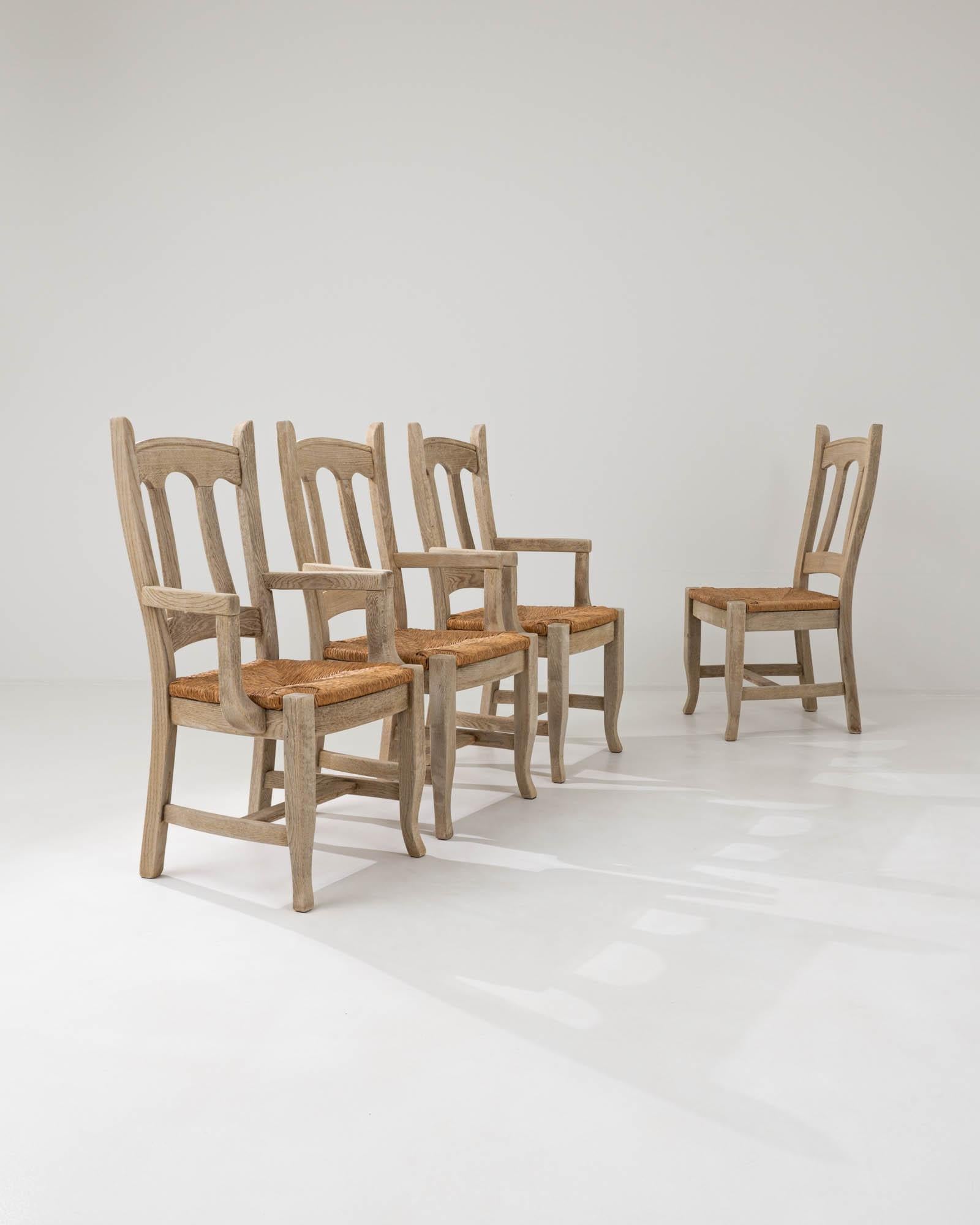 Handcrafted in Belgium in the 20th century, this set of four dining chairs showcases a gracefully flowing silhouette shaped by subtly inclined backrests and curved armrests that organically grow into the base with bent legs. The traditional slat