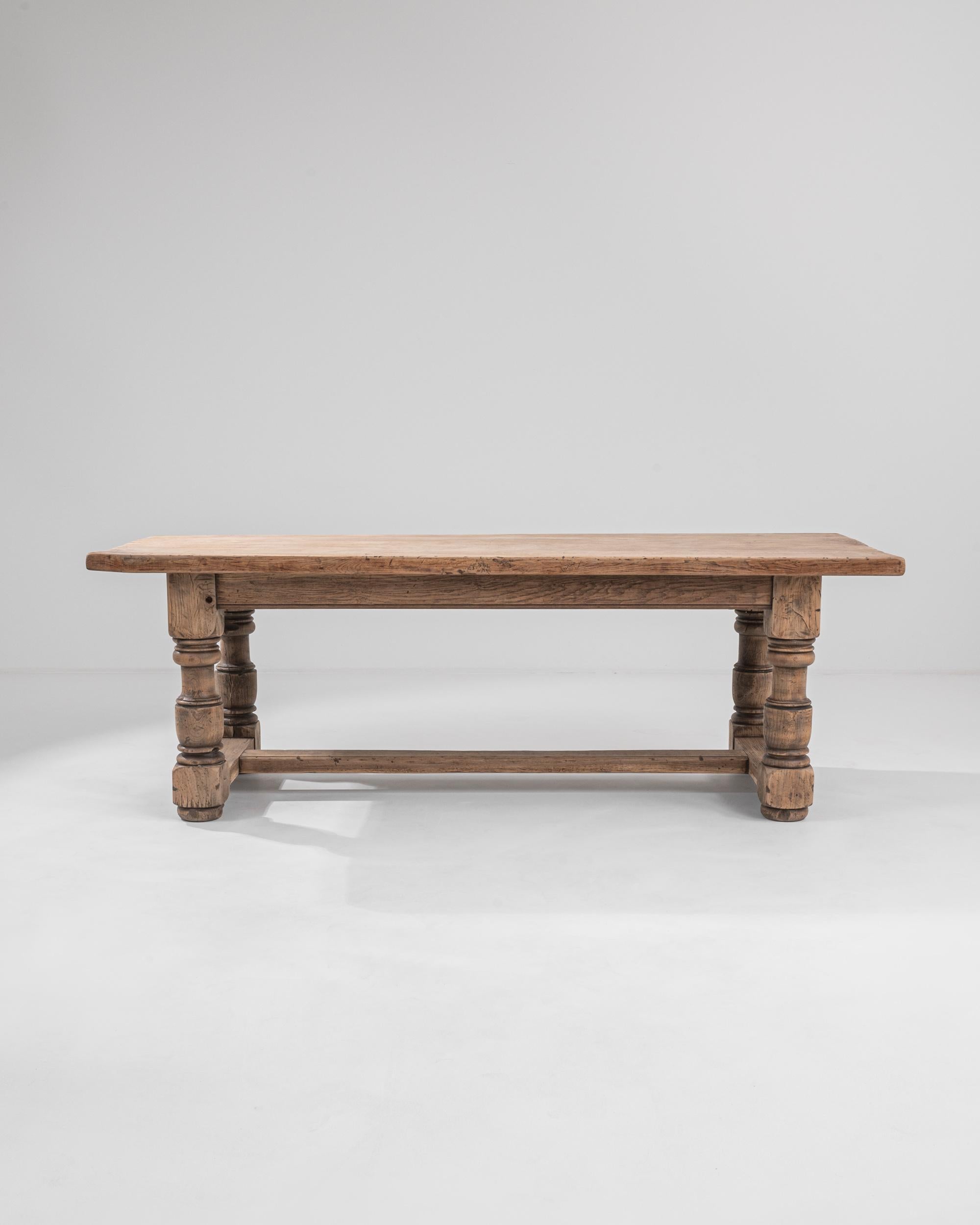A dining table from Belgium, circa 1950. The thick, sturdy planks of wood that form the table top and legs of this monumental trestle table exude a calming sense of earthy resilience. The legs of this table have been sumptuously lathed into finely