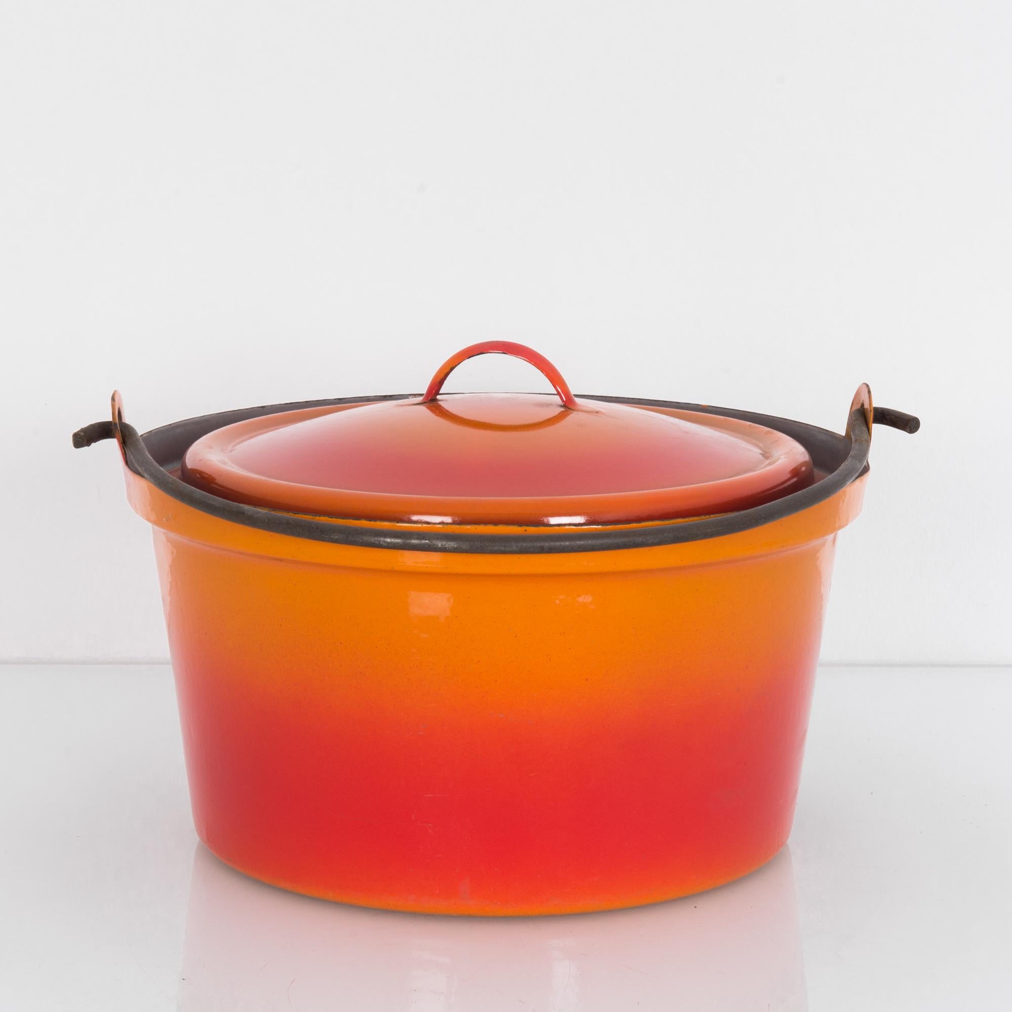 The red-orange gradient of this large enamel pot makes it a striking decorative piece for your interior space. Made in Belgium, the pot comes with a lid and a simple, black carrying handle.