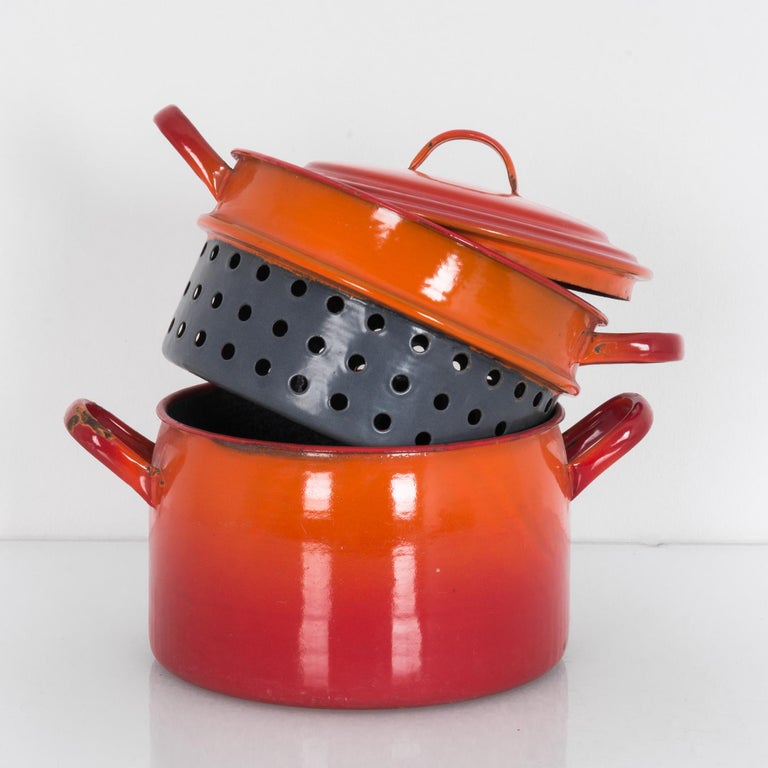A vintage enameled metal pot with lid and pasta strainer from Belgium. Features a glossy orange-red gradient vibrant like June-July sunset. A practical pot for boiling pasta or preparing the Moules of Moules-Frites. Buttery brine of swimming