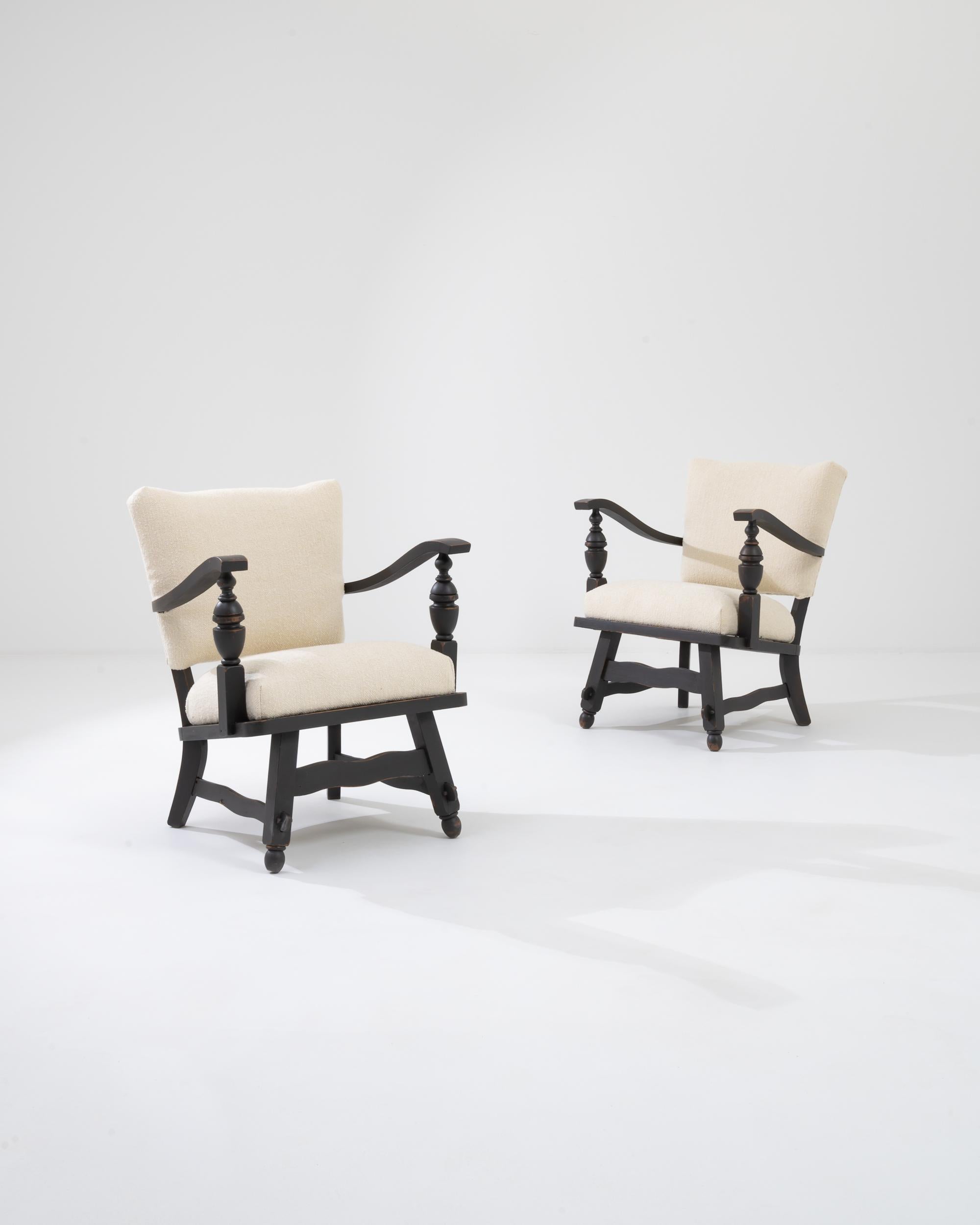 A pair of wooden upholstered armchairs from 20th century Belgium. Sculptural supports have been expertly turned on a lathe, dramatically swooping arms, and gently waving legs further define these charming farmhouse style chairs. Their sturdy,