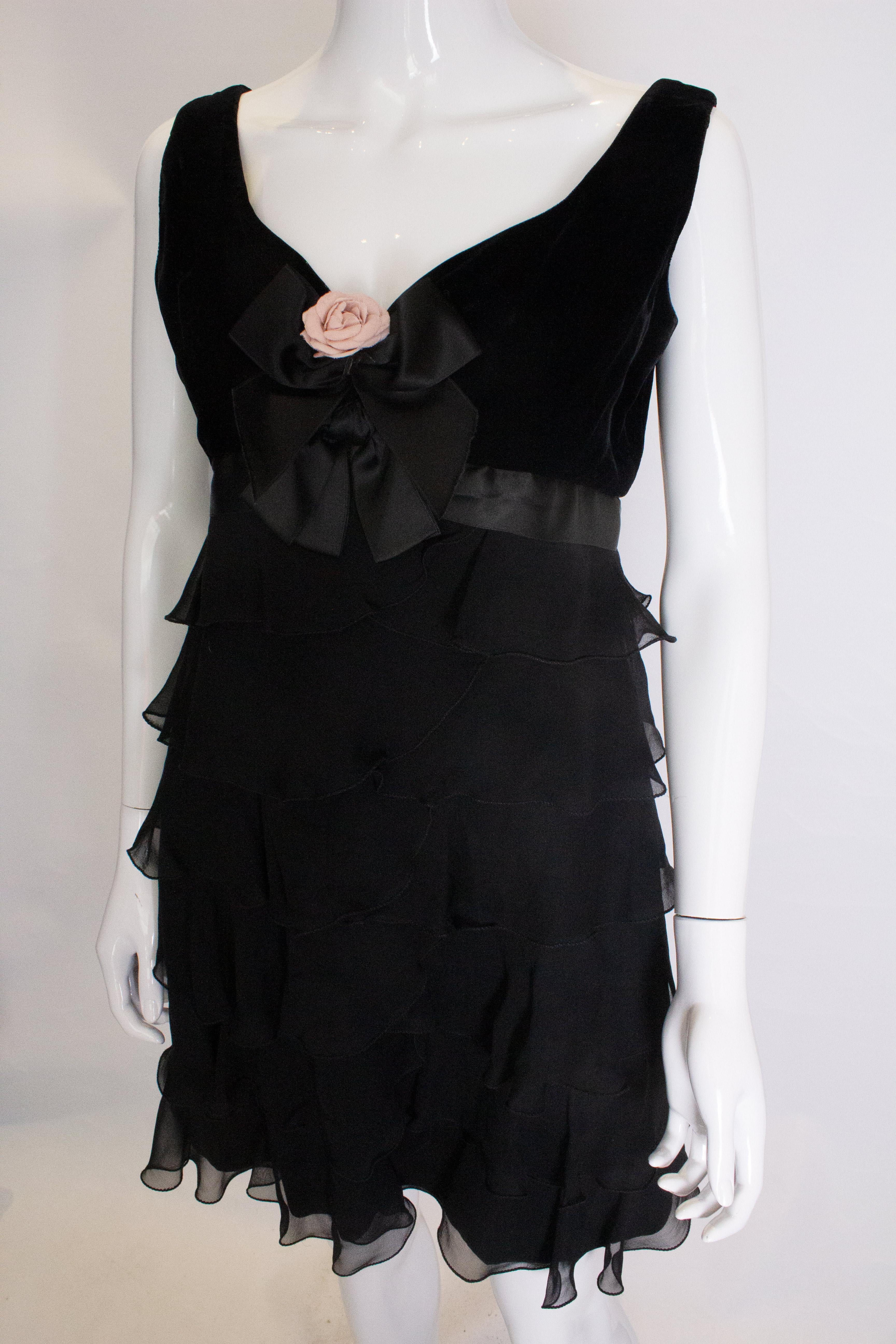 A chic black cocktail dress by Bellville Sassoon/Lorcan Mullany.The dress hasa v neckline and scoop backline  in silk velvet. The skirt area is layers of black silk over a black sheath. It has a central back zip.