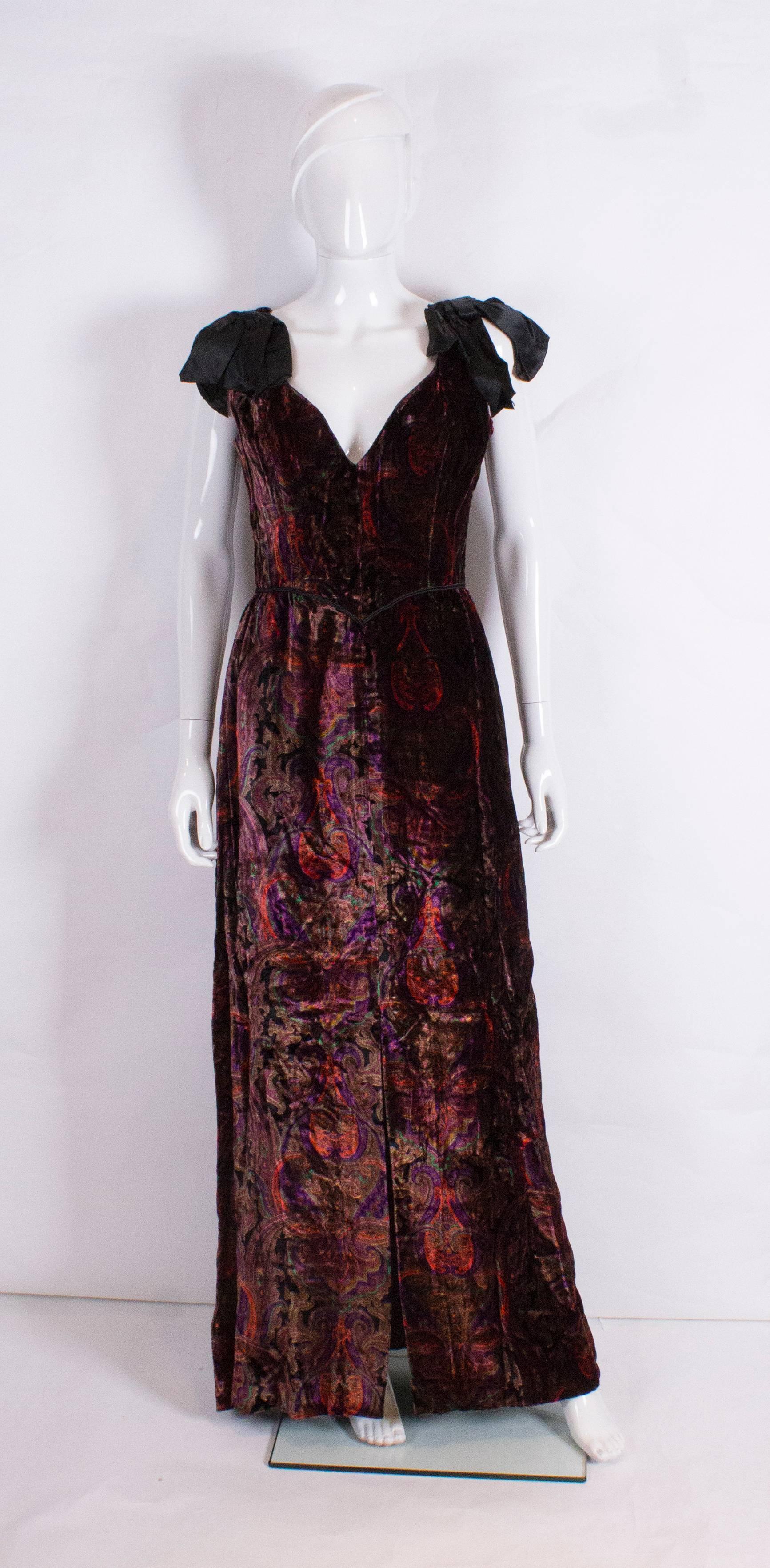 A great vintage gown by Bellville Sassoon. In a silk velvet paisley like print, the colours include, purple, green, red and black.  The dress has a v neckline, black trim at waist leval , 23'' slit at the front and a central back zip plus bows on