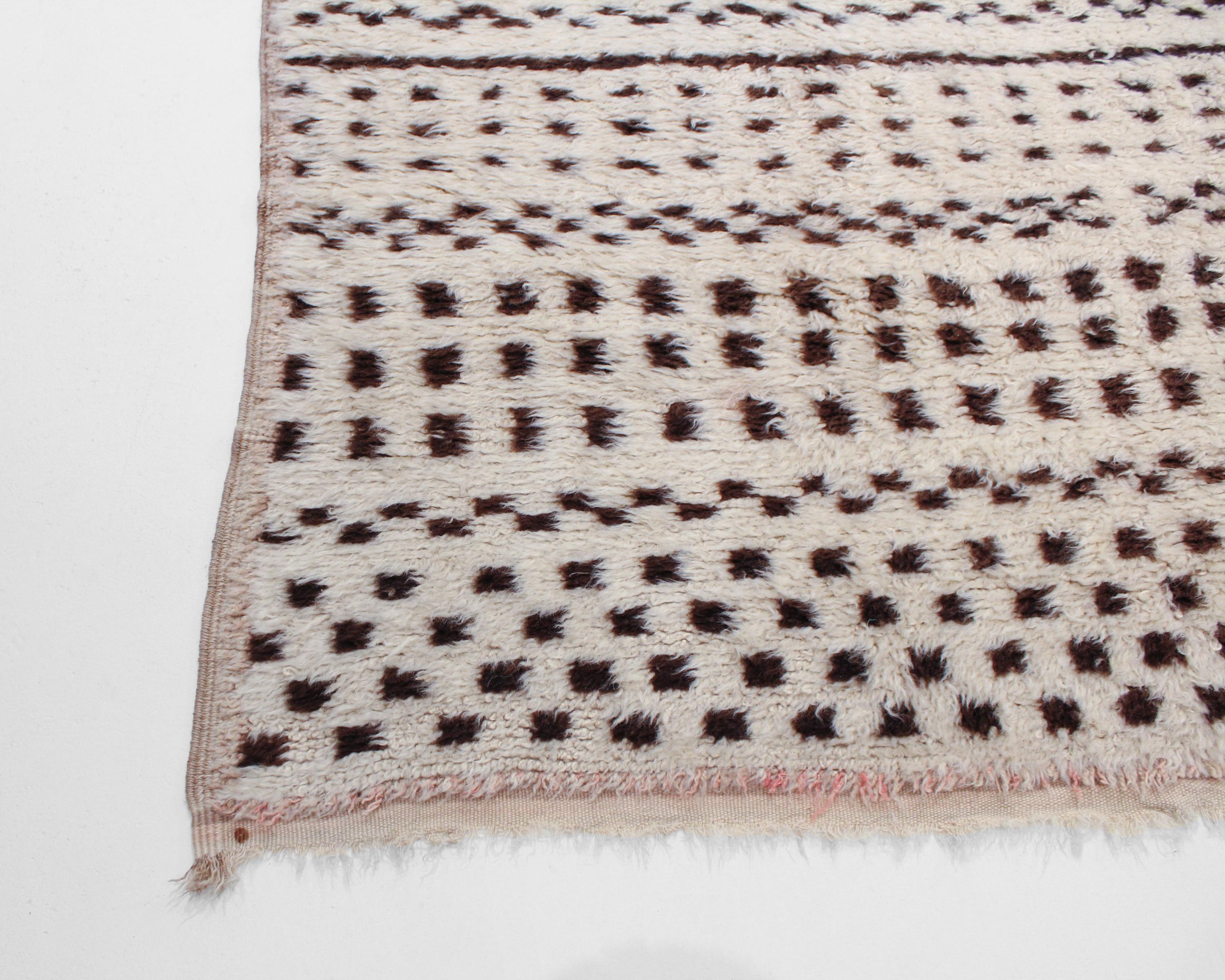With incredible detail and texture, this hand knotted wool vintage Beni Ourain Moroccan rug is a captivating vision of woven beauty. Characterized by the broad ivory field that is representative of Beni Ourain, along with the eye-catching