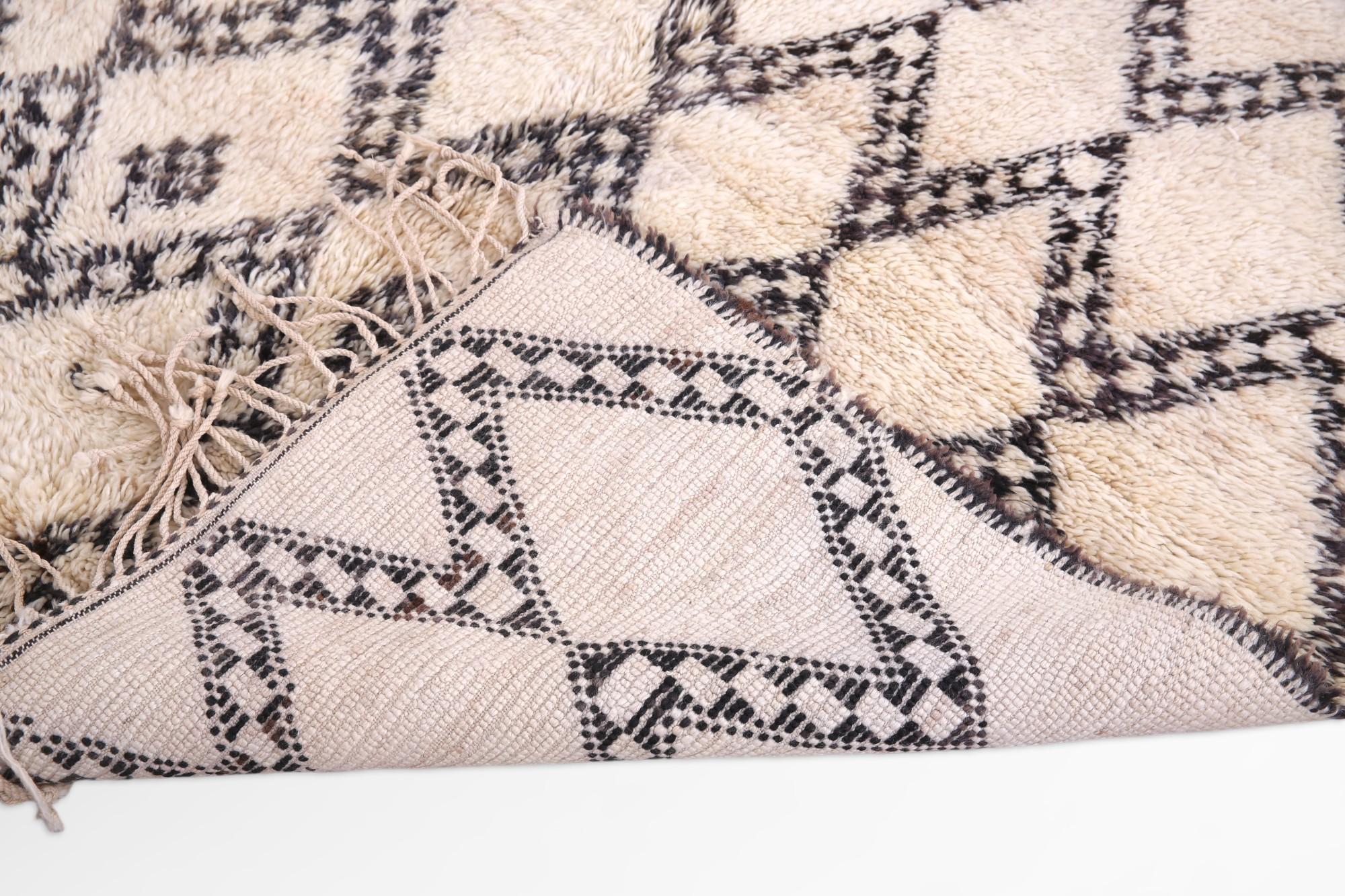 Dieser marokkanische Teppich, der von den Kunsthandwerkern des Beni Ourain-Stammes in sorgfältiger Handarbeit gewebt wurde, ist ein Zeugnis der nomadischen Eleganz und der detaillierten Handwerkskunst seiner Schöpfer. Die kühnen Linien und das